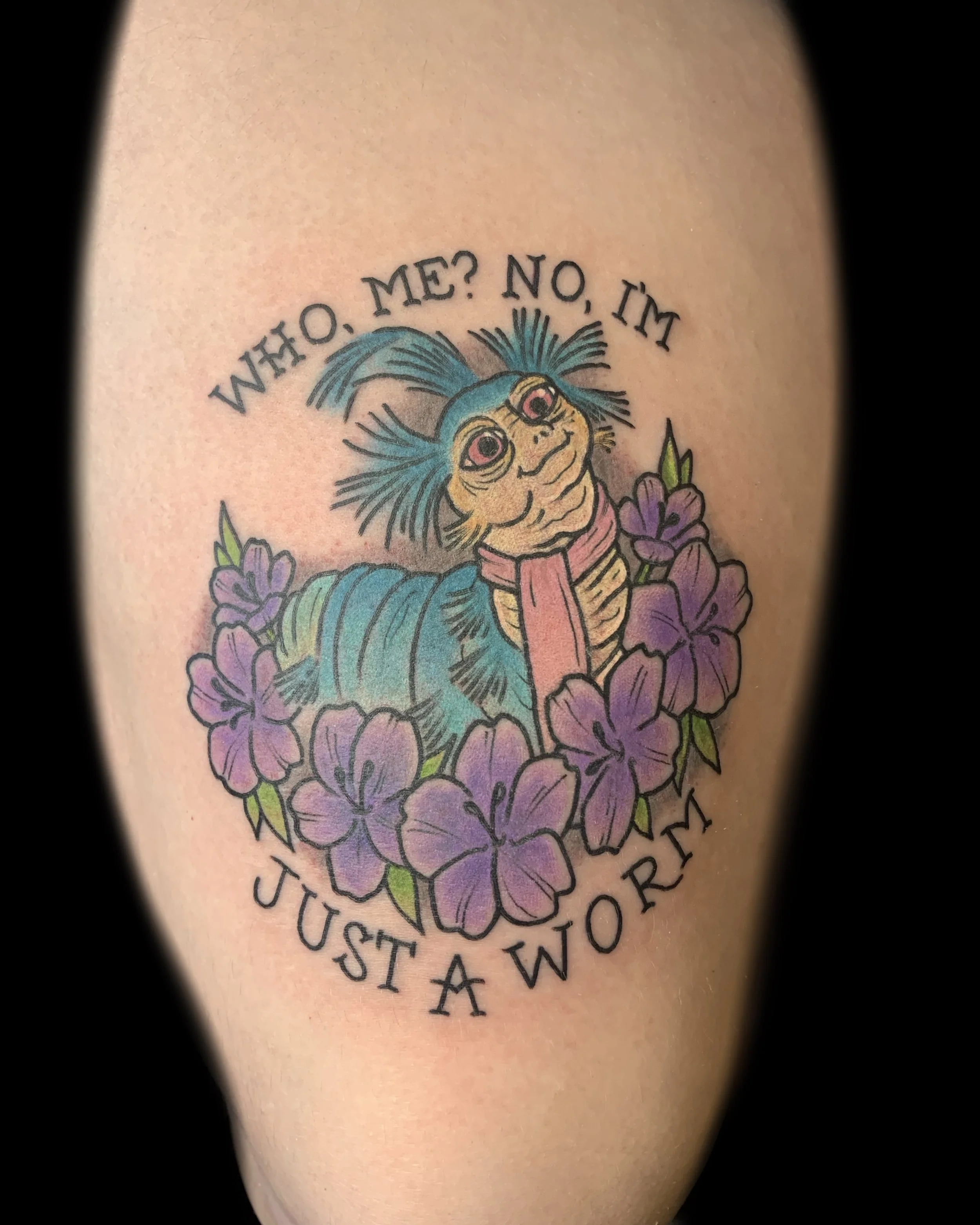 Colorful tattoo of a Caterpillar with flowers and text reading 'Who, me? No, I'm just a worm.'