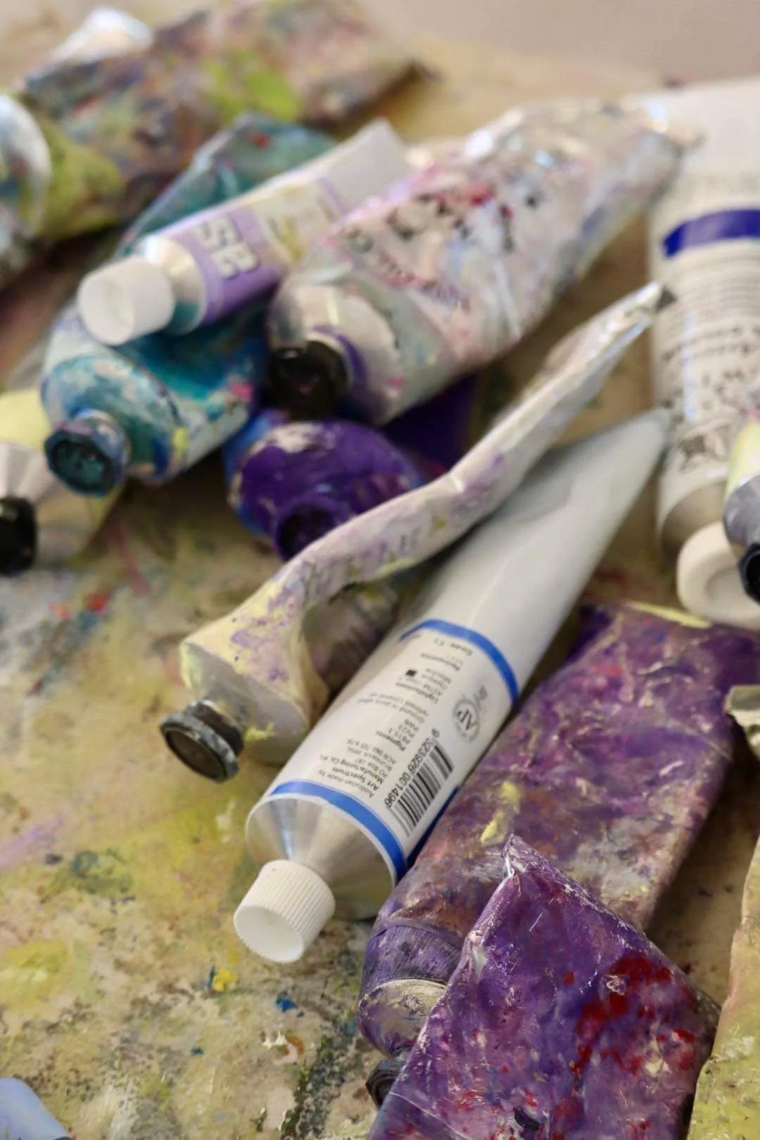 A collection of used, paint-splattered tubes of acrylic paint on a messy surface.