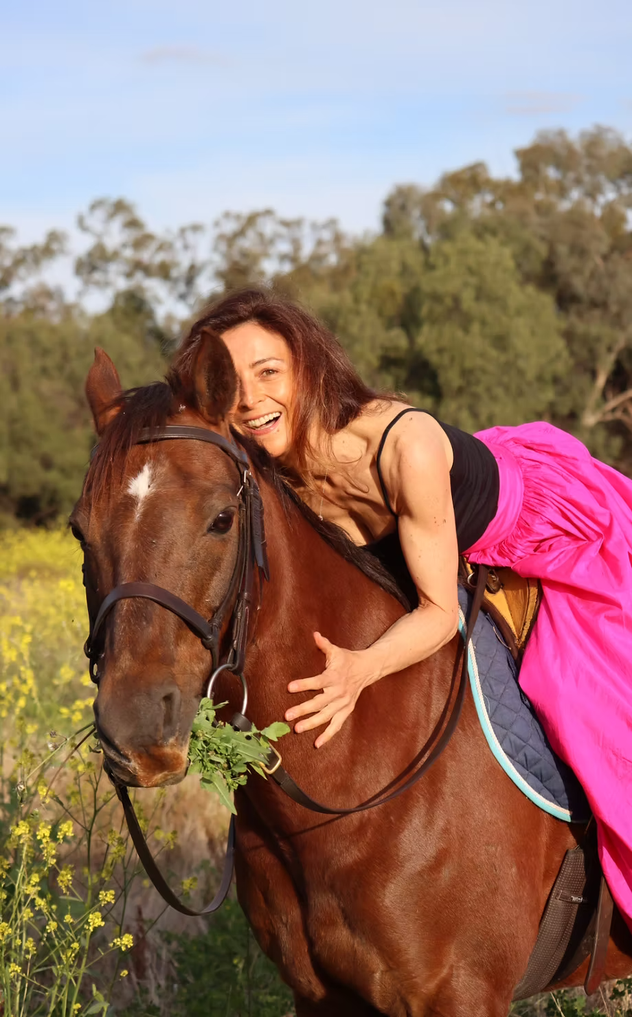Jamila in a pink skirt riding a horse in a field of wildflowers