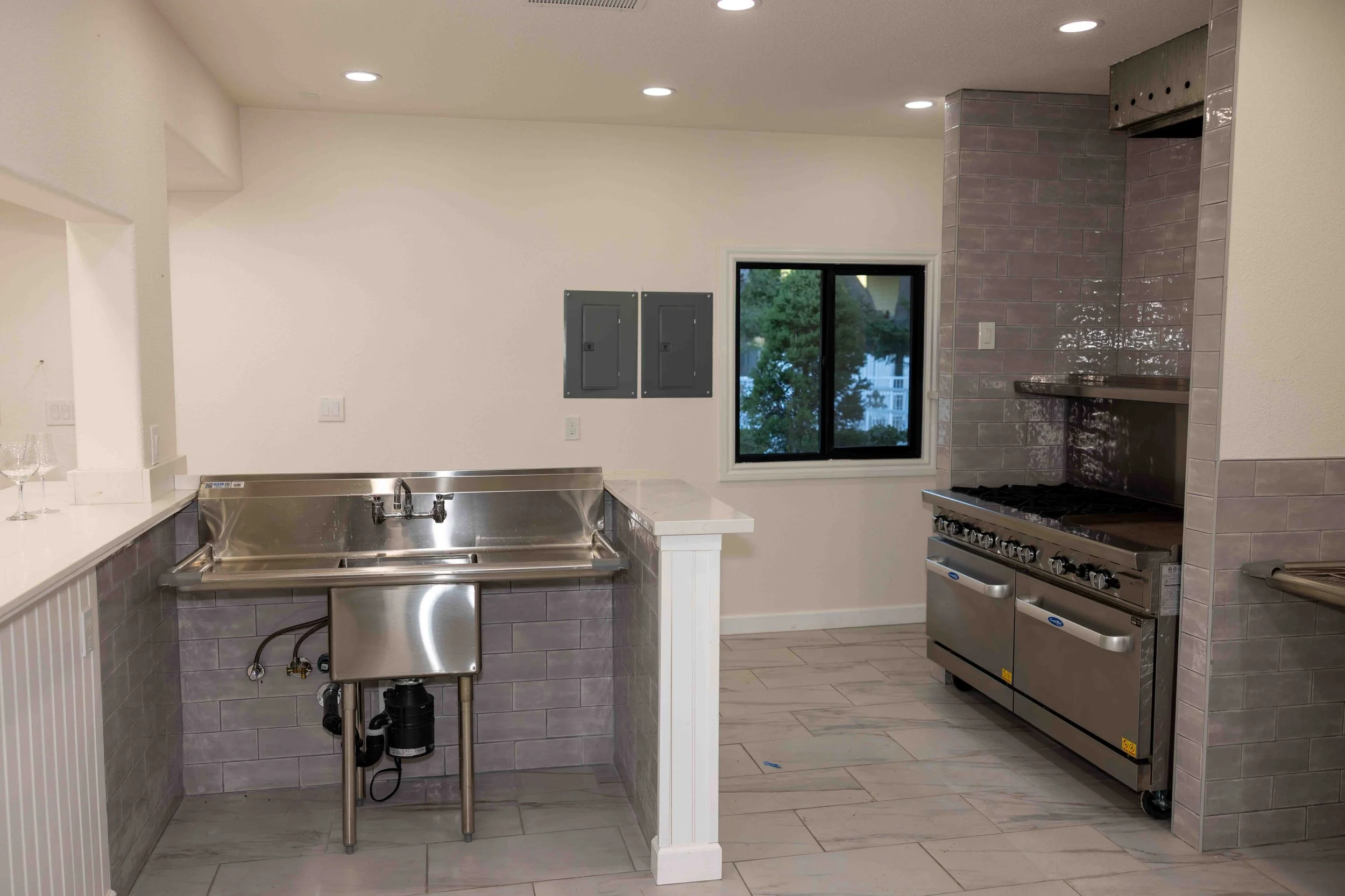 Kitchen with stainless steel sink, gas stove, window, and electrical panels on the wall.