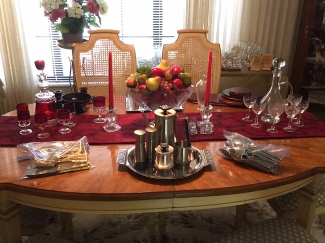 Dining table set for a meal with red candles, glassware, a fruit centerpiece, and decorative items.