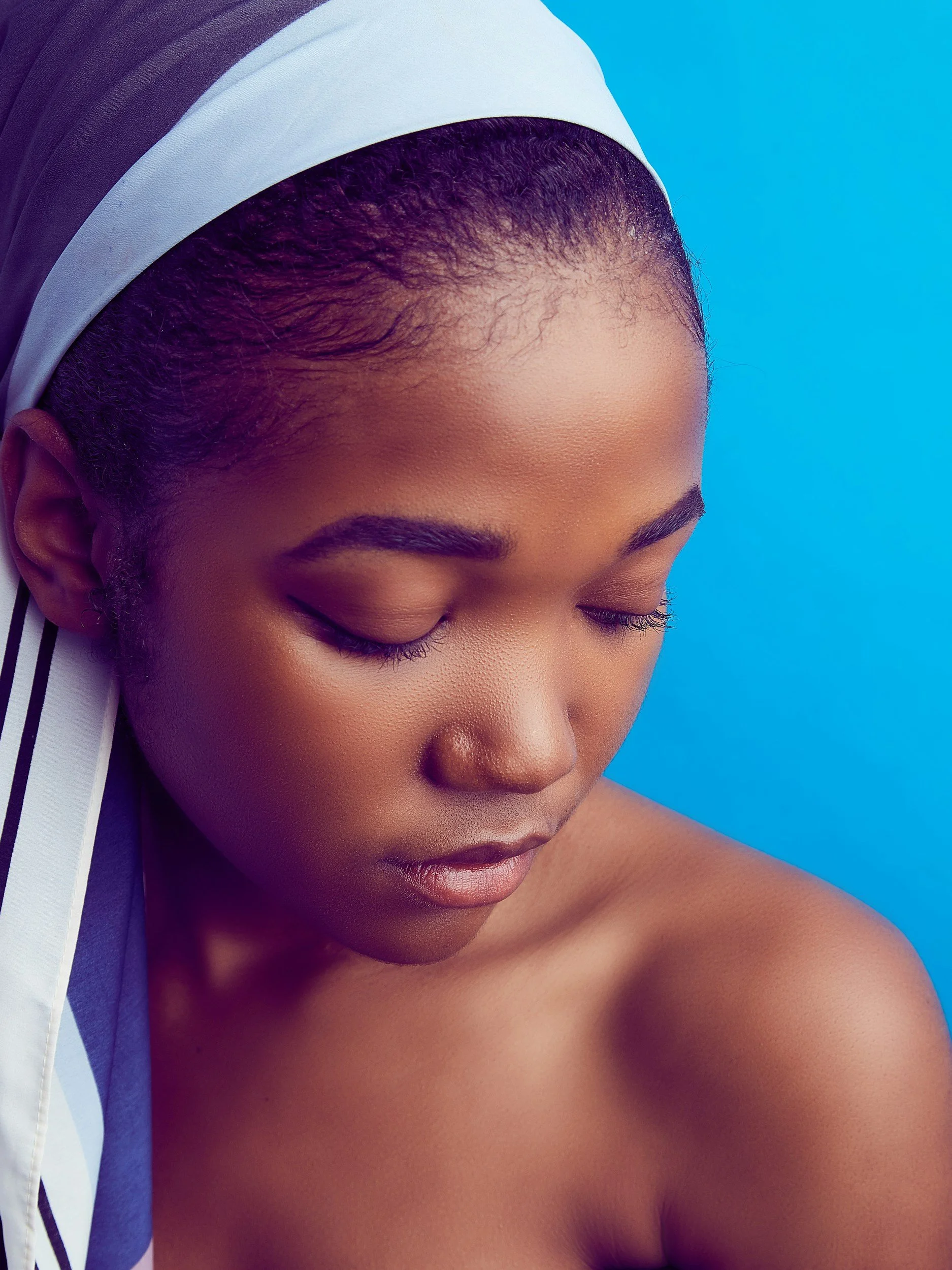 Close-up portrait of a woman with closed eyes and smooth skin against a blue background.