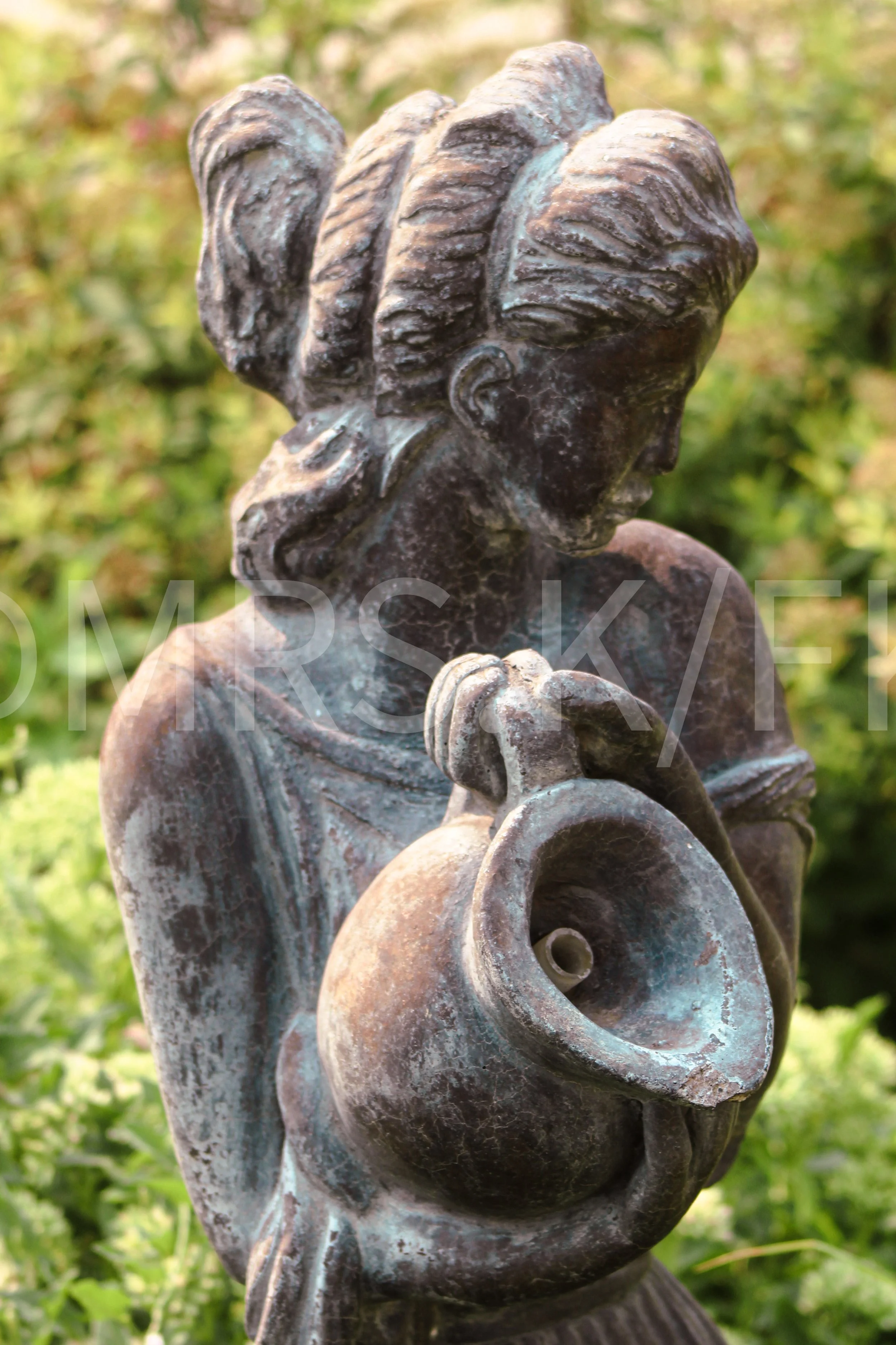 An Original Piece of Photography 1 of 10 to print Custom Fine Art - Close-up of a bronze sculpture of a woman with styled hair, holding a spiral shell in her hands, outdoors with blurred greenery background.
