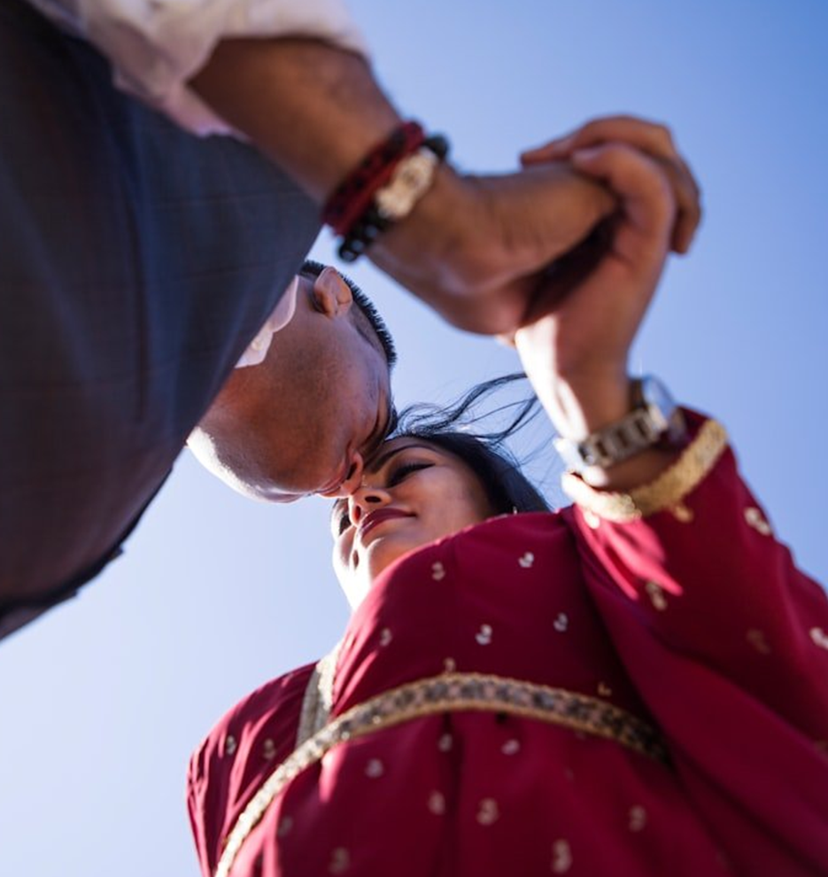 A couple holding hands and touching foreheads under a clear blue sky.