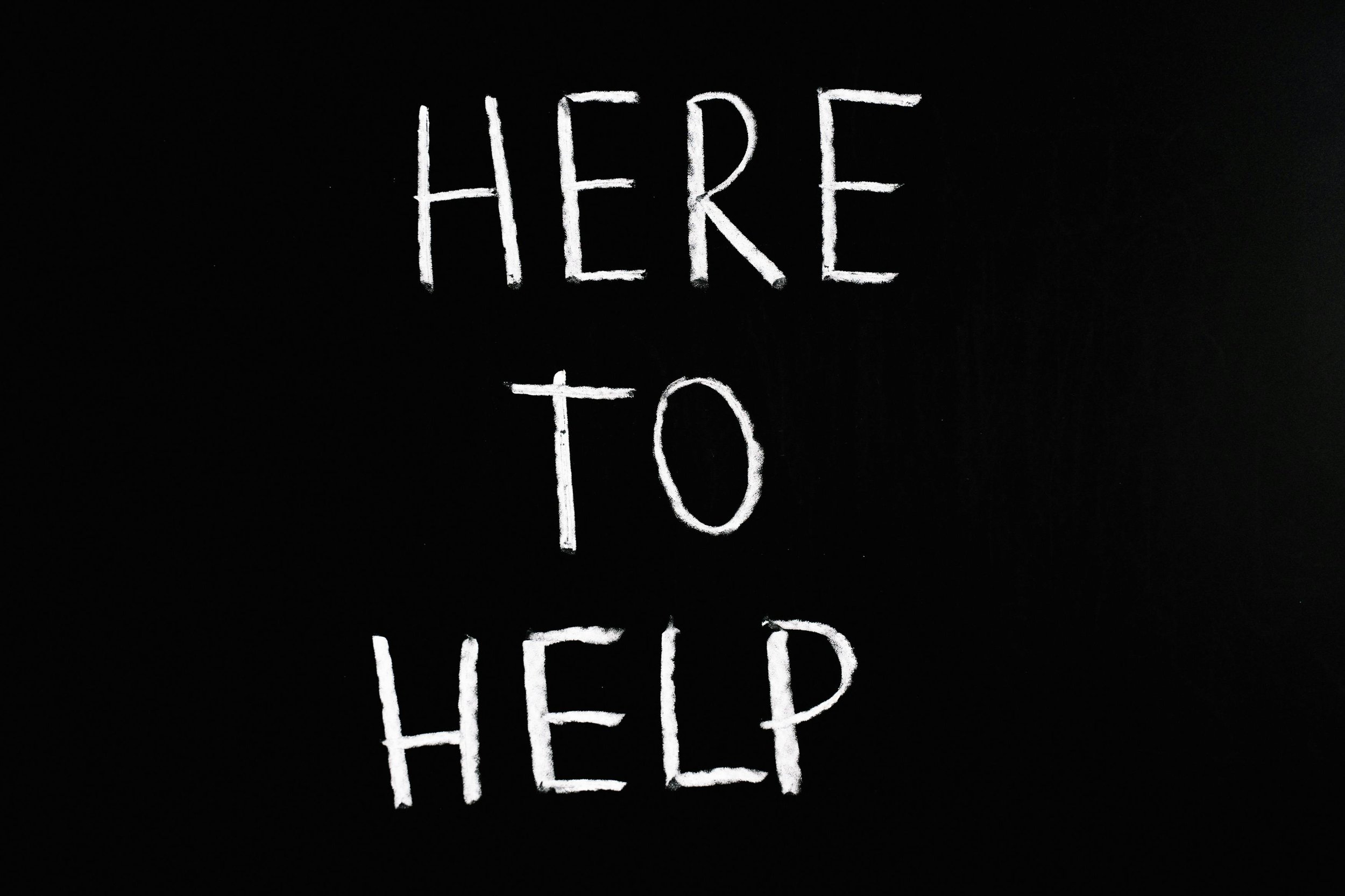 Black background with white chalk-like handwritten text that reads, "HERE TO HELP".