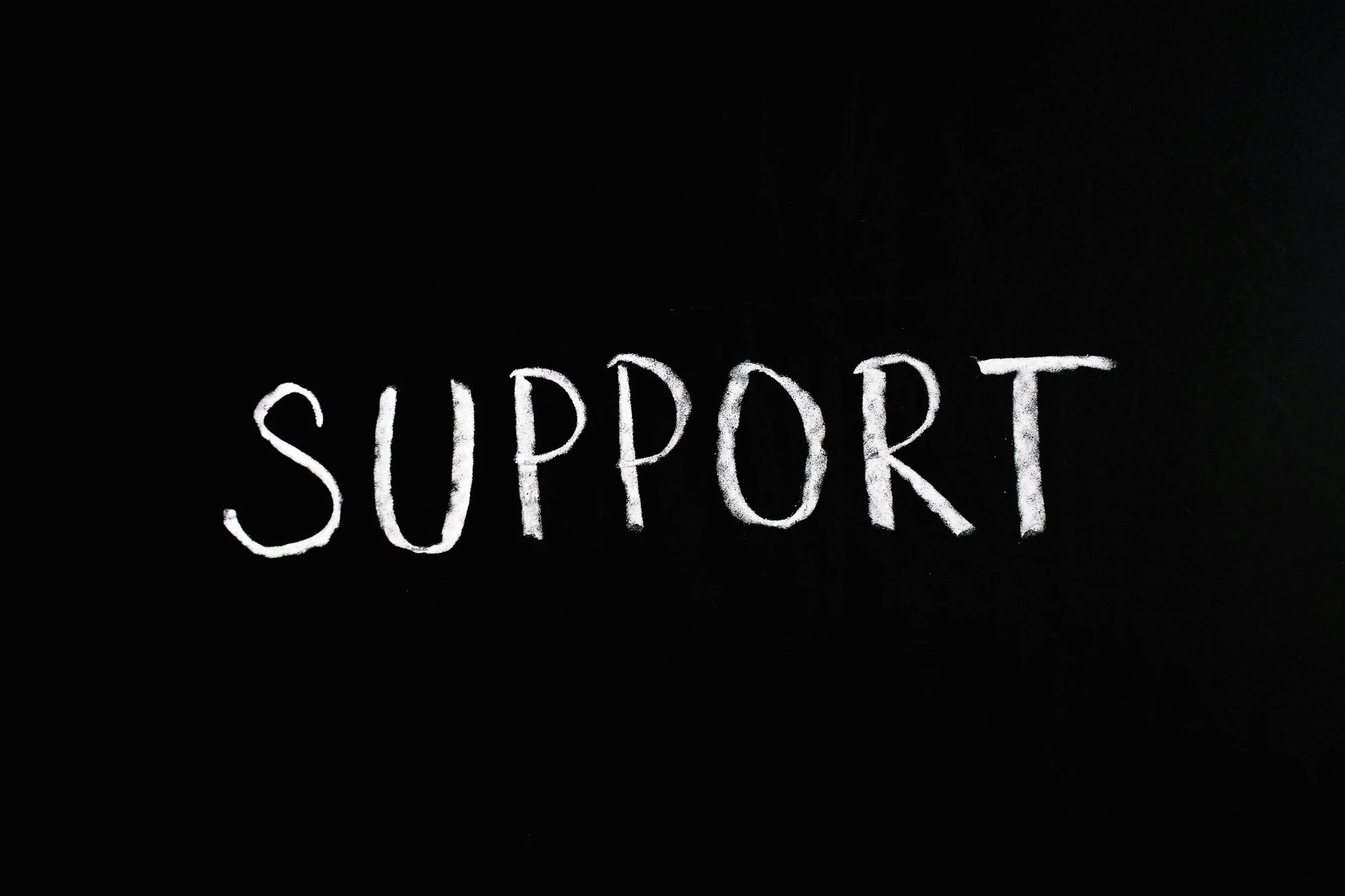 The word 'SUPPORT' written in white chalk on a black surface.