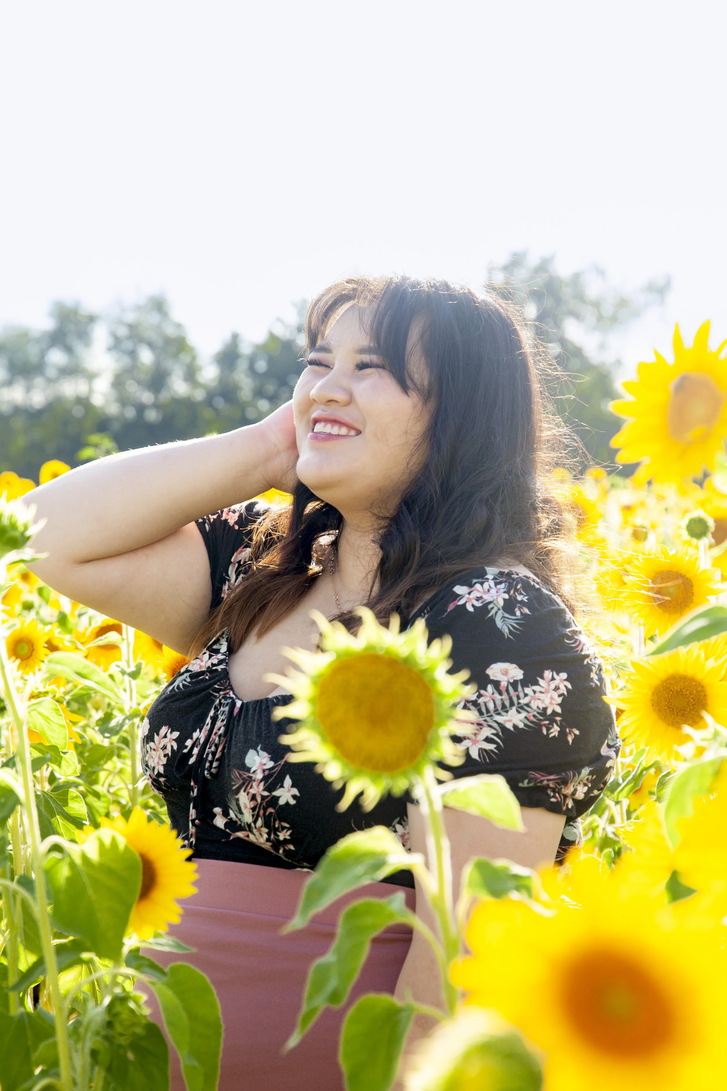 Young Hmong woman smiling in a sunflower field on a sunny day.