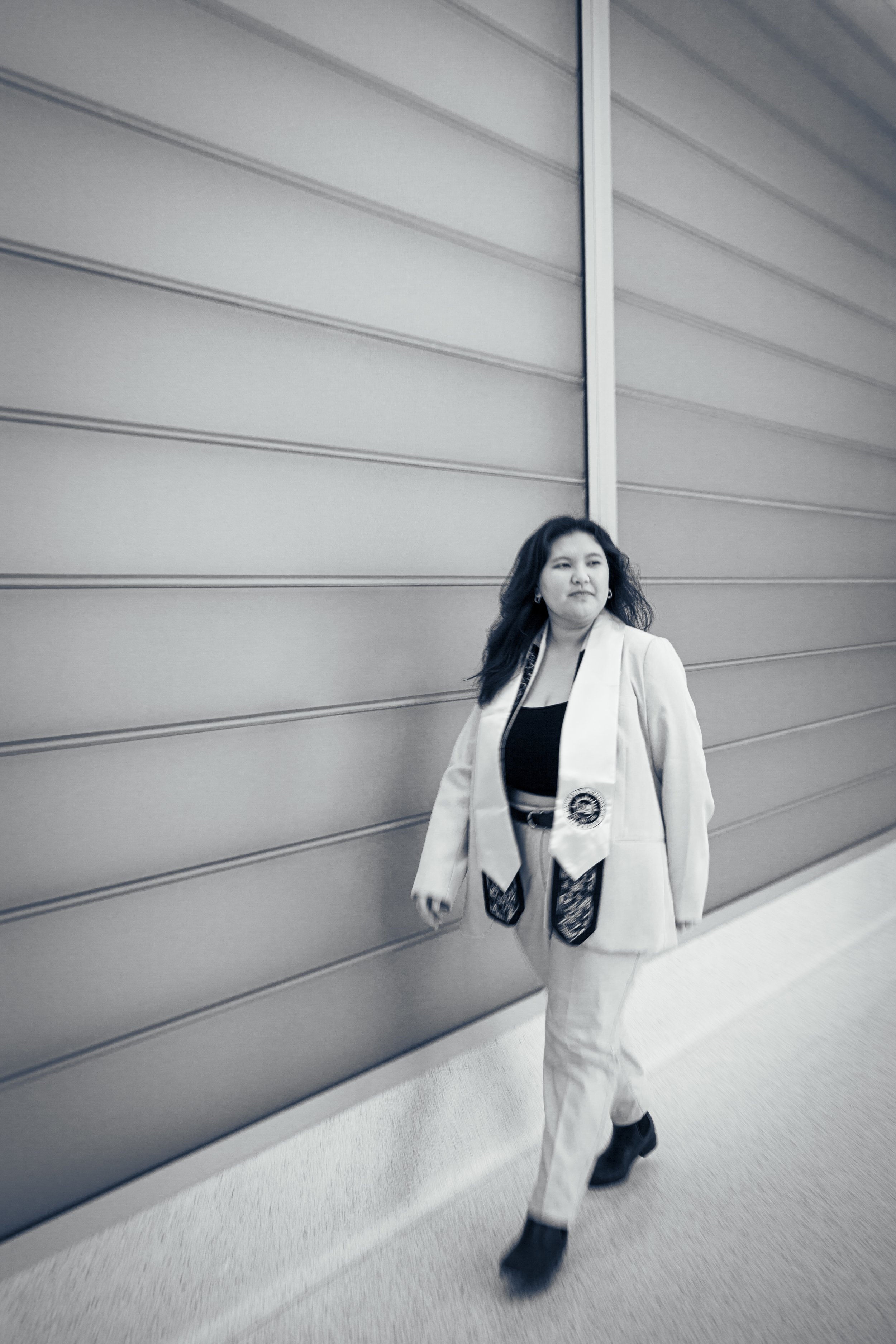 A Hmong woman dressed in a white tuxedo and black top walking indoors.