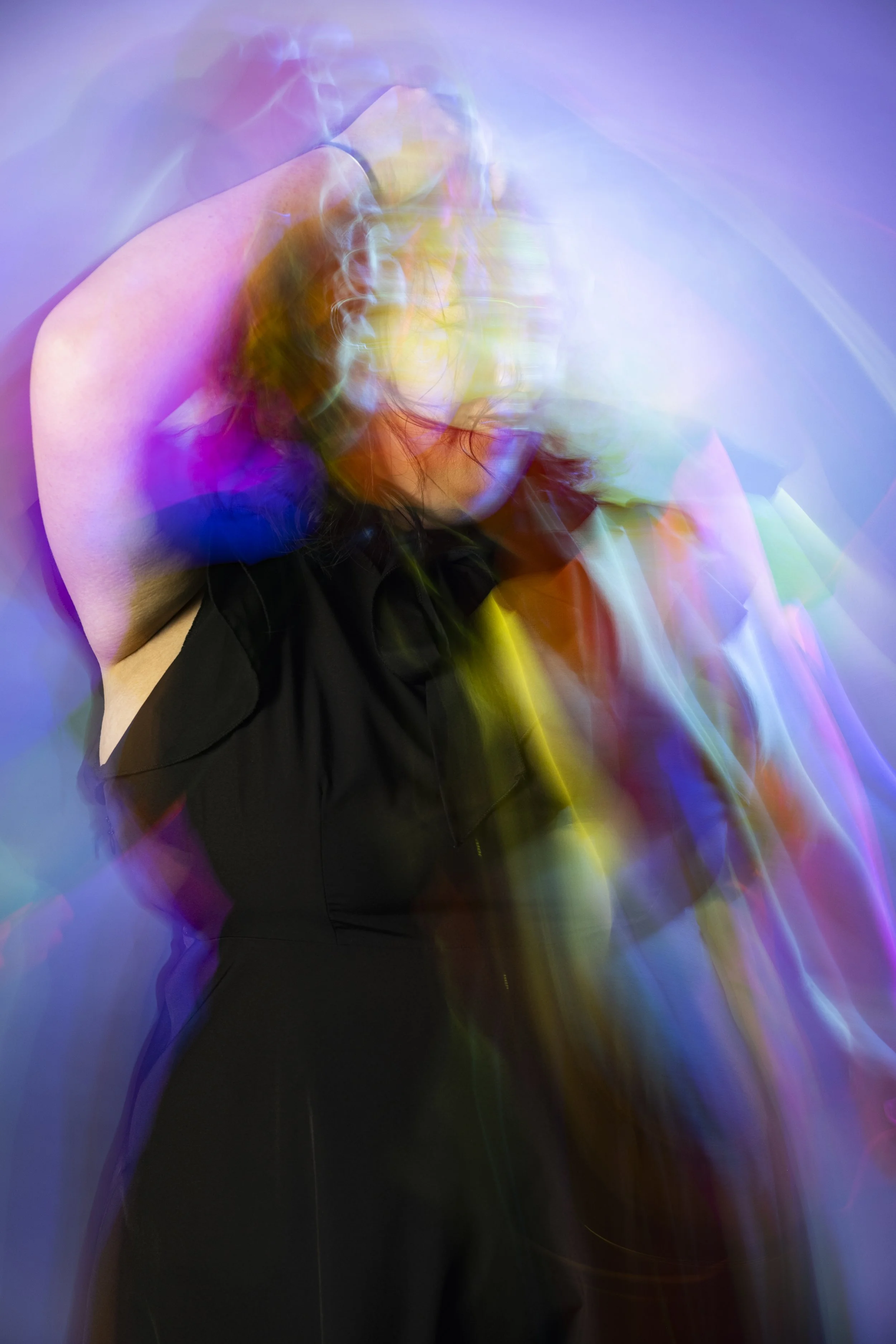 A Hmong woman with dark hair in a black outfit is moving in front of a colorful background, creating a blurred and layered effect.