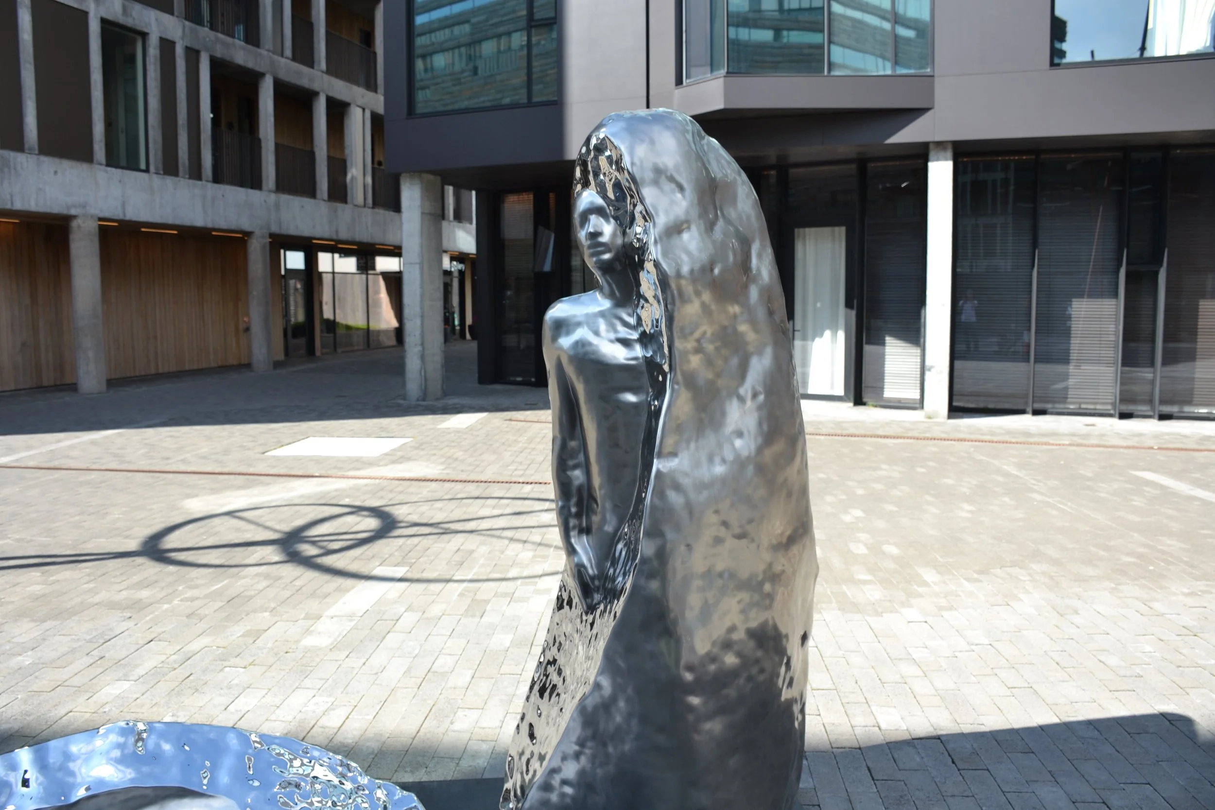 Polished stainless-steel figure of Imprint reflecting the surrounding buildings and sky in Hafnartorg, Reykjavík.