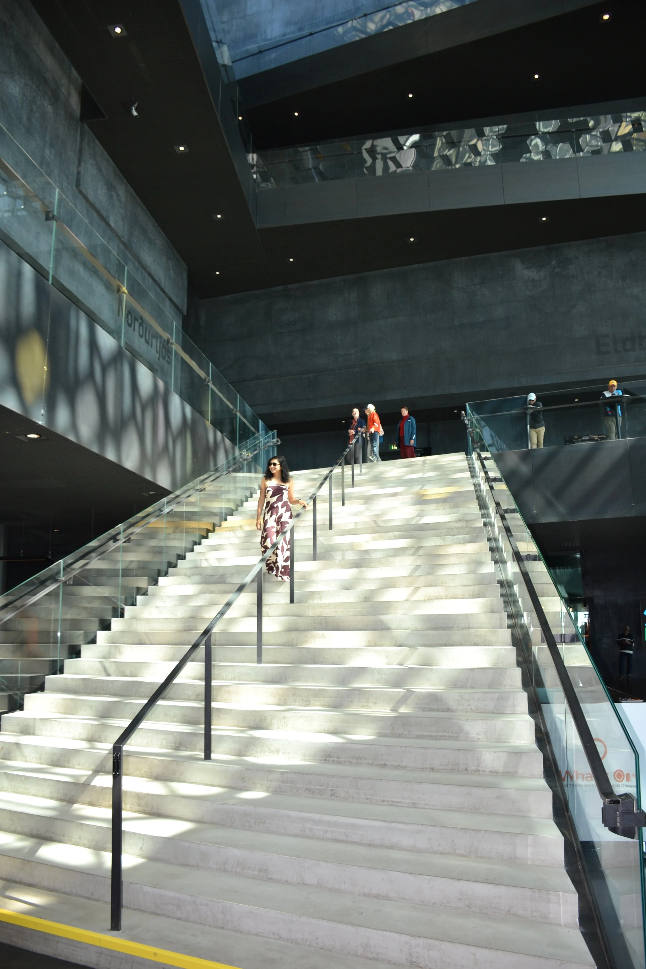 Mirrored geometric ceiling above exposed concrete walls and glass railings inside Harpa Concert Hall.