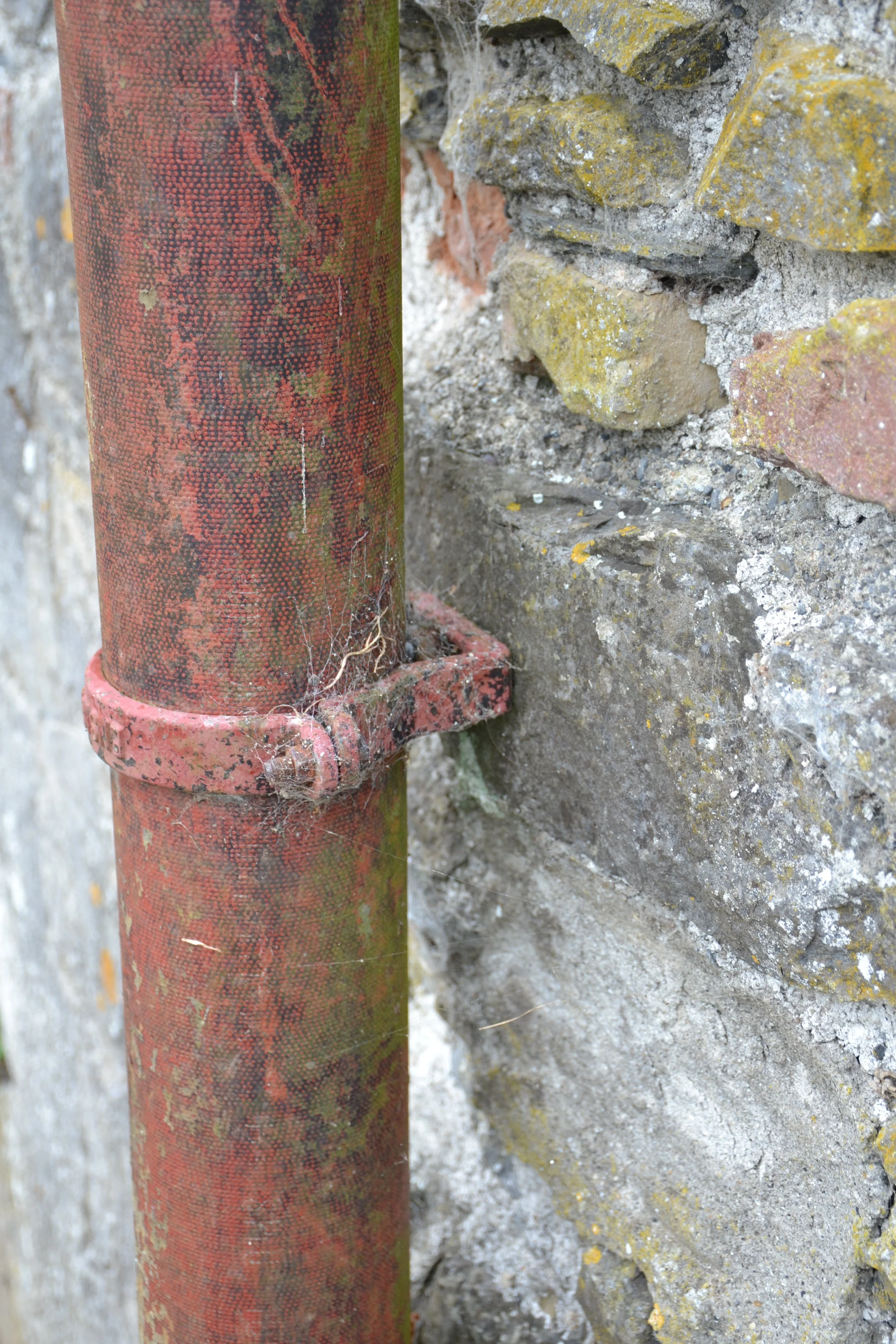 Weathered painted-metal downpipe and bracket attached beside historic stone masonry at Kilkenny Castle.