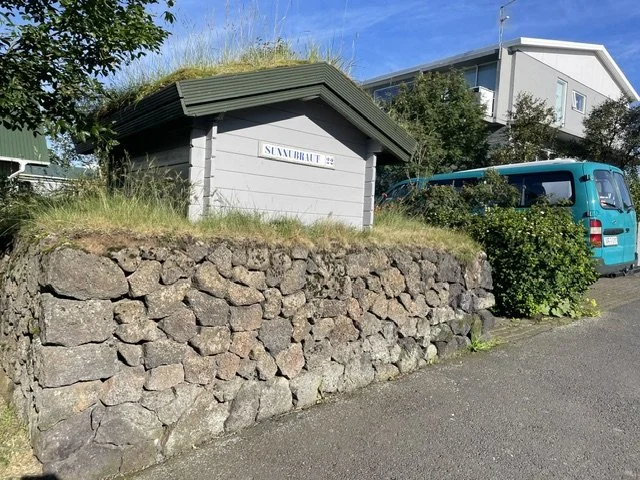 A residential stone wall with carefully placed stone, supporting a small animal shelter with a green roof