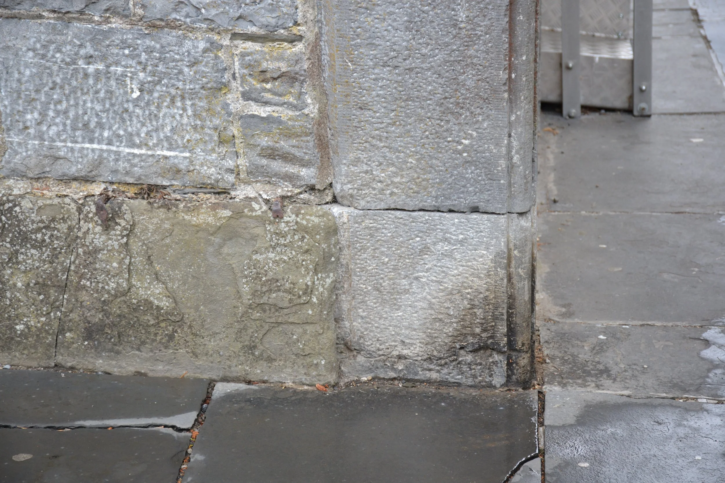 Deterioration at the base of a dressed-stone entrance surround at Kilkenny Castle beside masonry and paving.