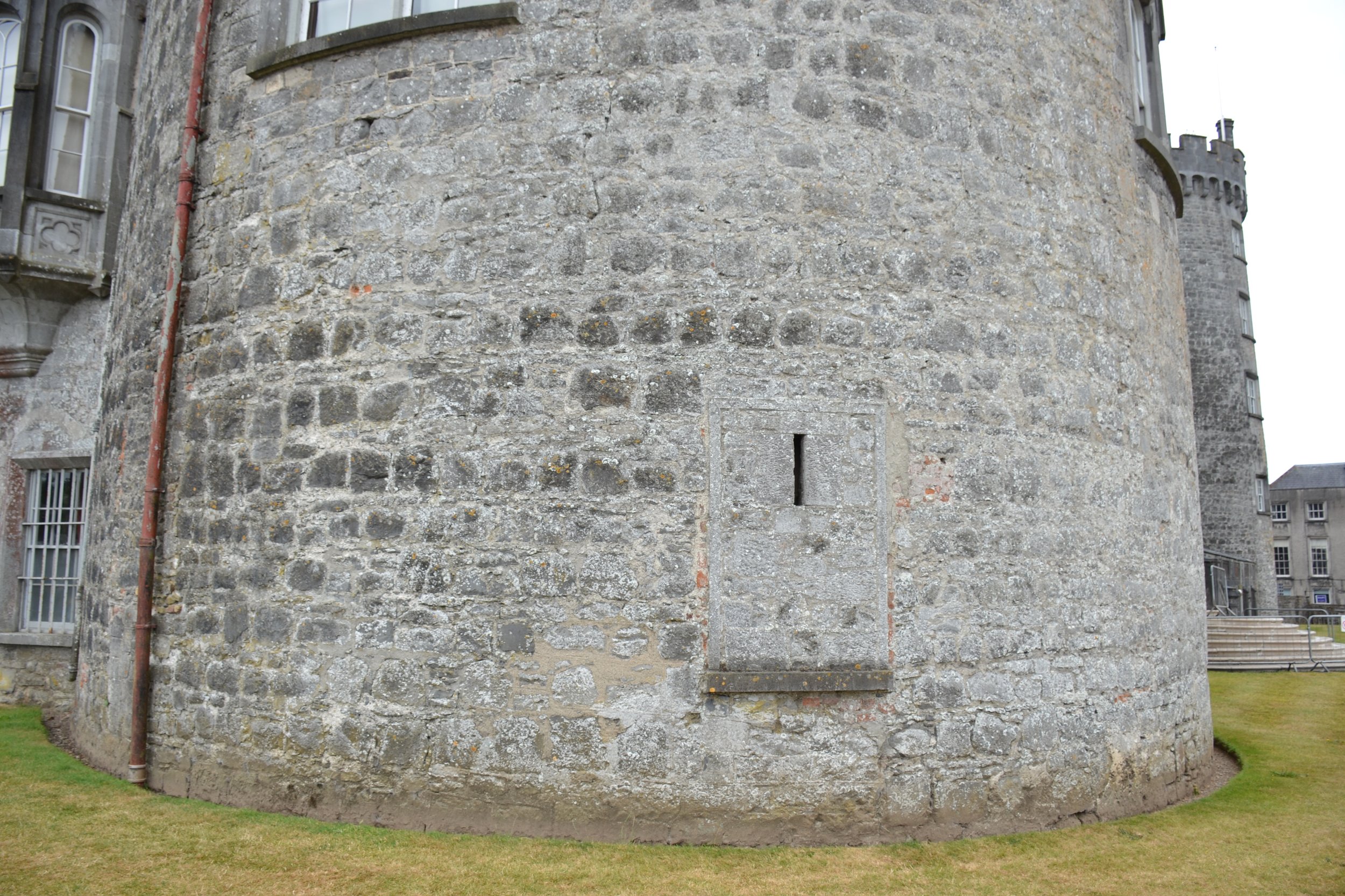 Close view of a round stone tower at Kilkenny Castle showing historic masonry, varied mortar joints, localized repairs, biological growth, and a former opening filled with stone.