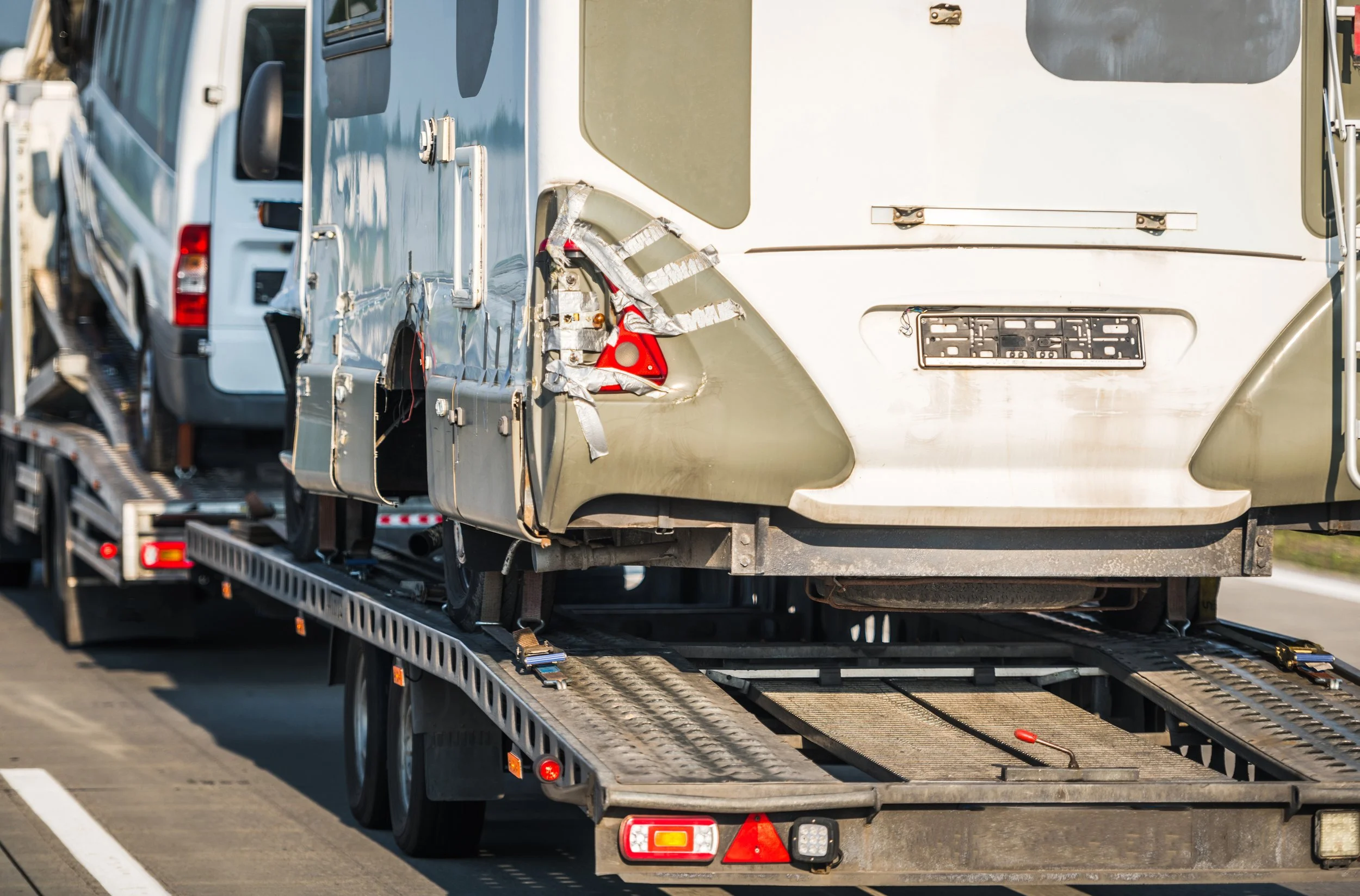 A damaged RV sits on the back of a tow truck