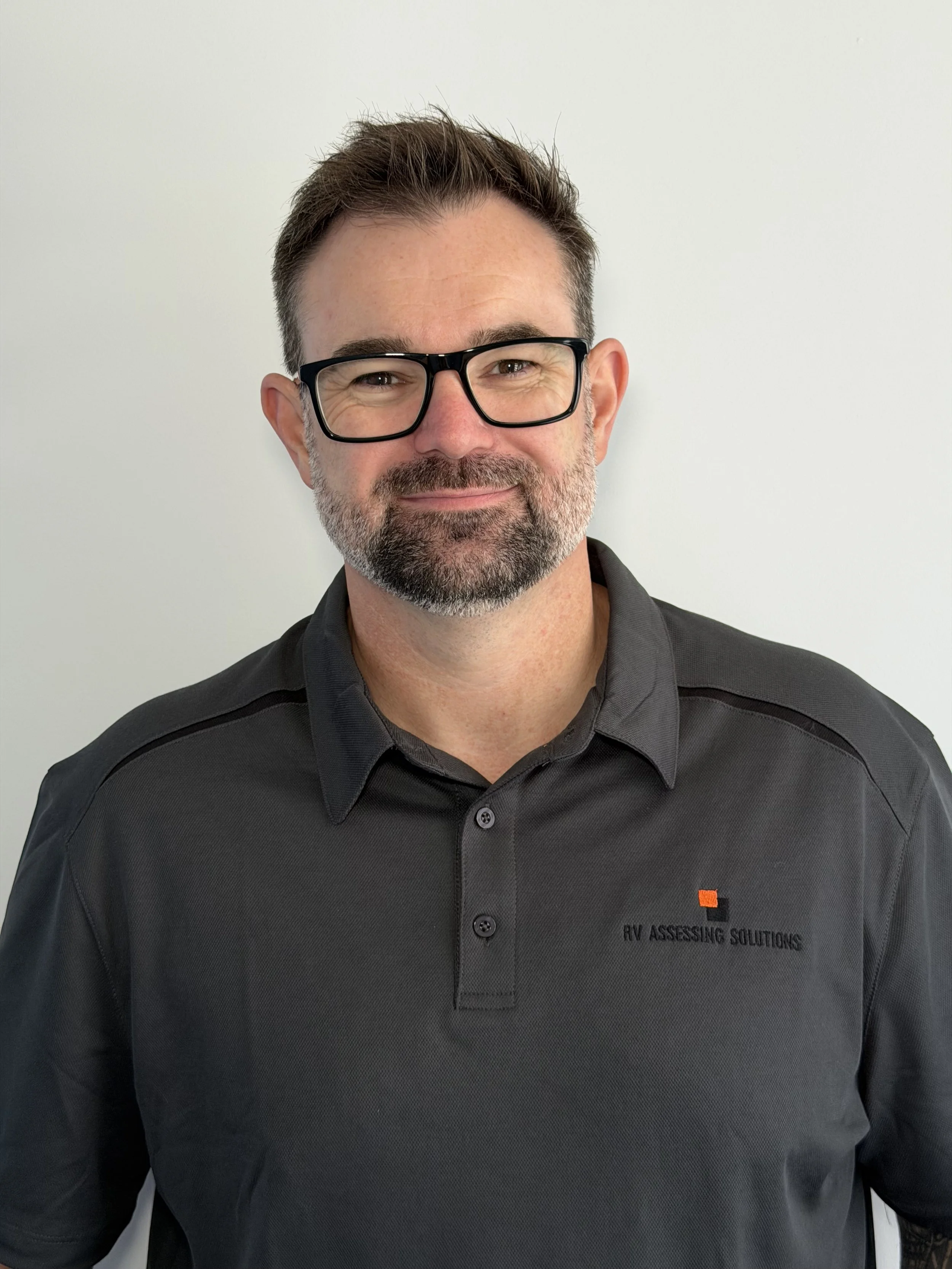 Adam Scobie smiles warmly wearing  a grey polo shirt and glasses