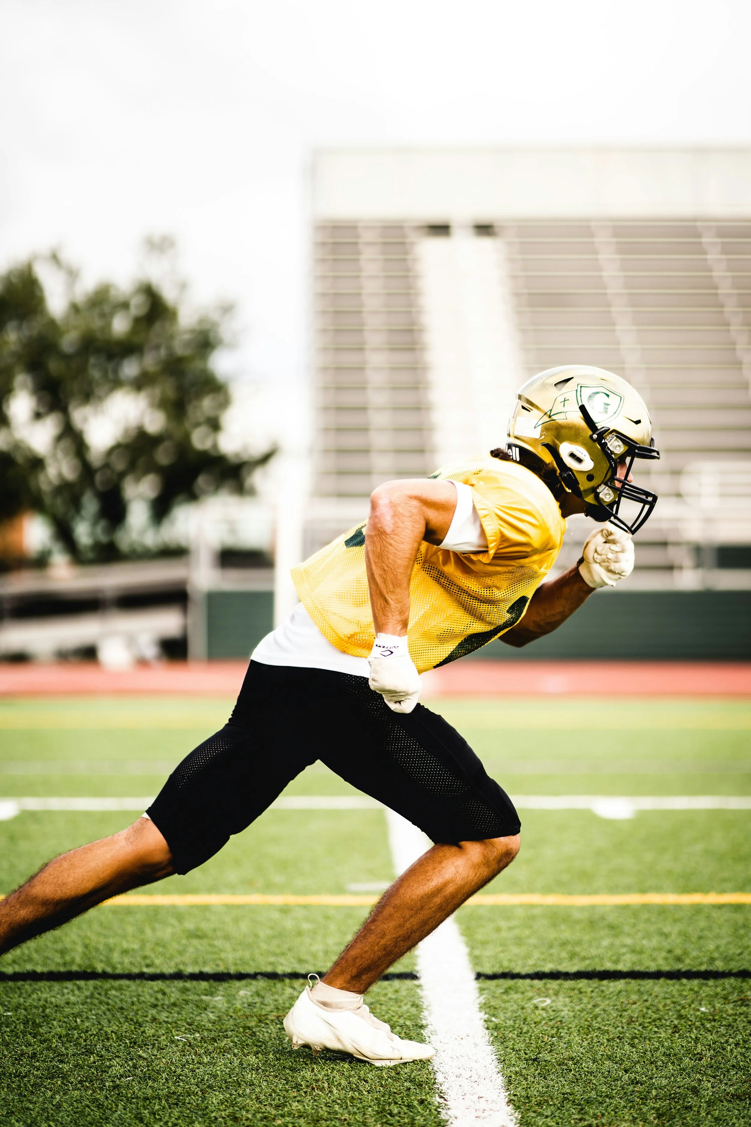 An American football player in yellow practice gear and a helmet is running on a football field.