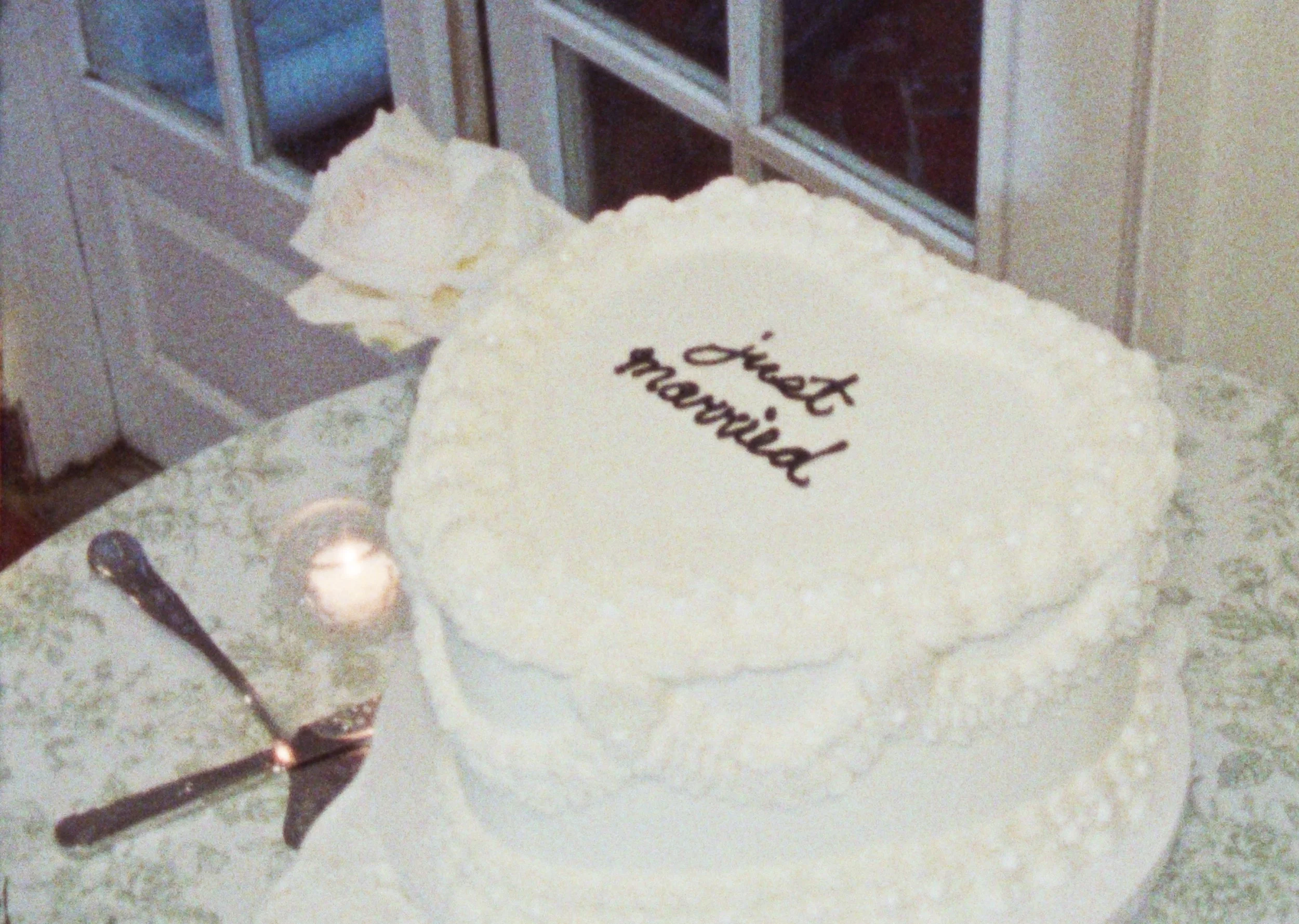 Close-up of a wedding cake with the words 'our wedding' written in black icing on top, placed on a countertop near a window.