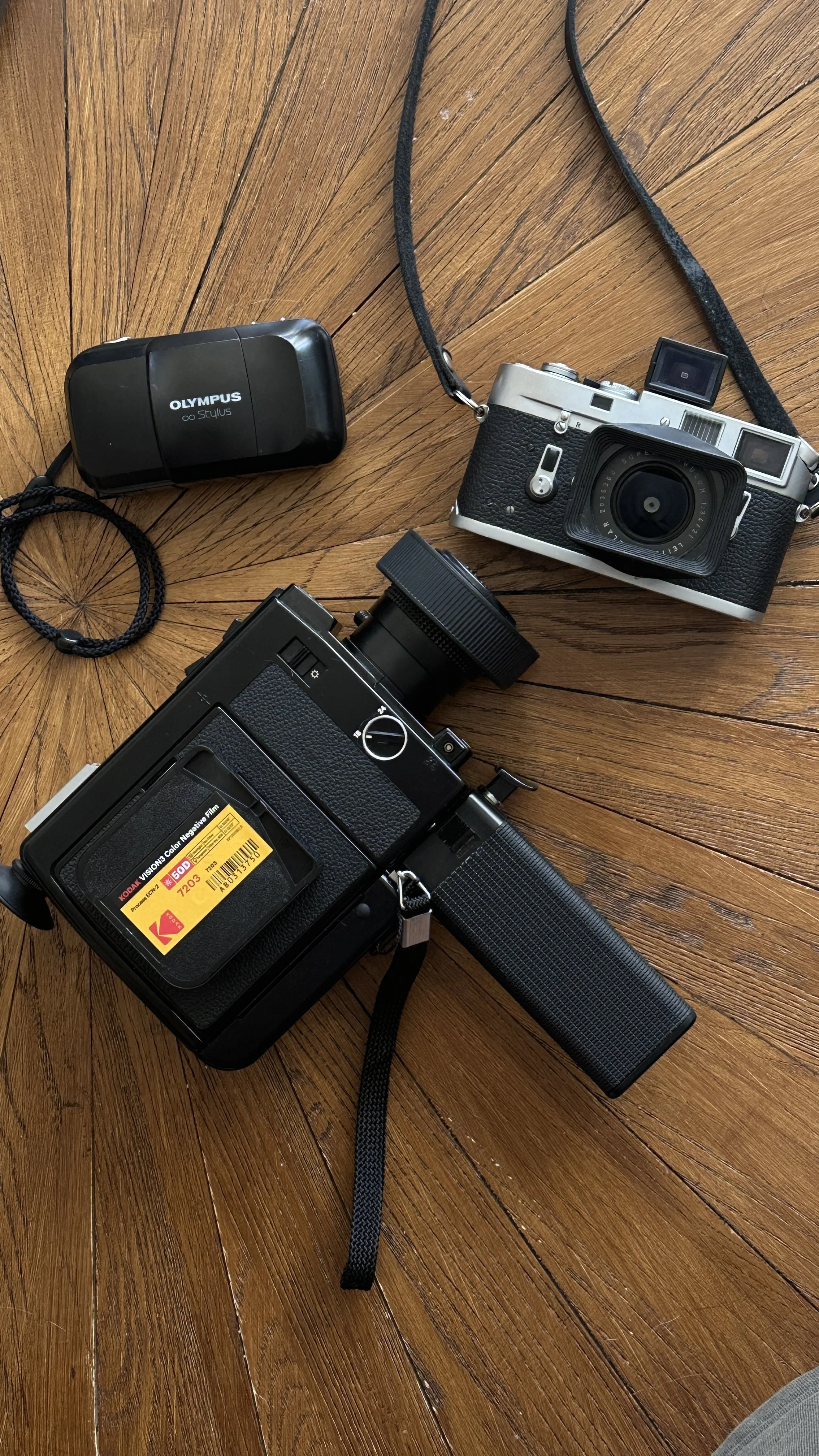 A collection of vintage cameras and accessories on a wooden surface, including two cameras, a lens, and a camera case.