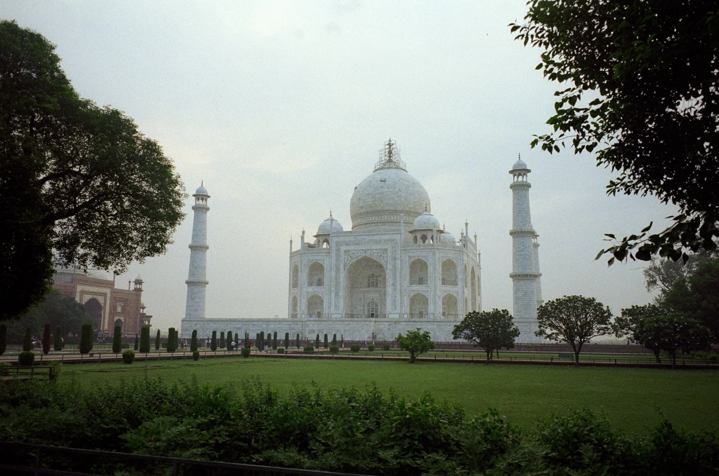 The Taj Mahal, a white marble mausoleum with a large central dome and four minarets, surrounded by green gardens and trees.
