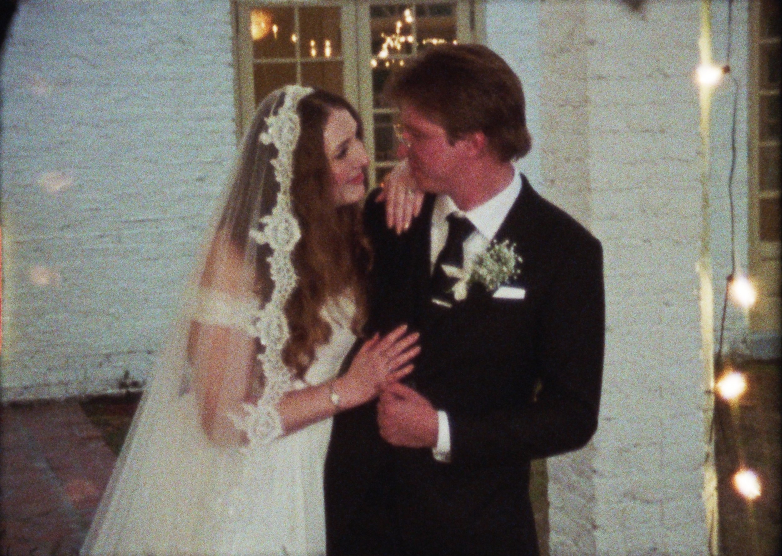 A bride and groom dancing closely at their wedding reception, with the bride in a white gown and lace veil, and the groom in a black tuxedo with a boutonniere.