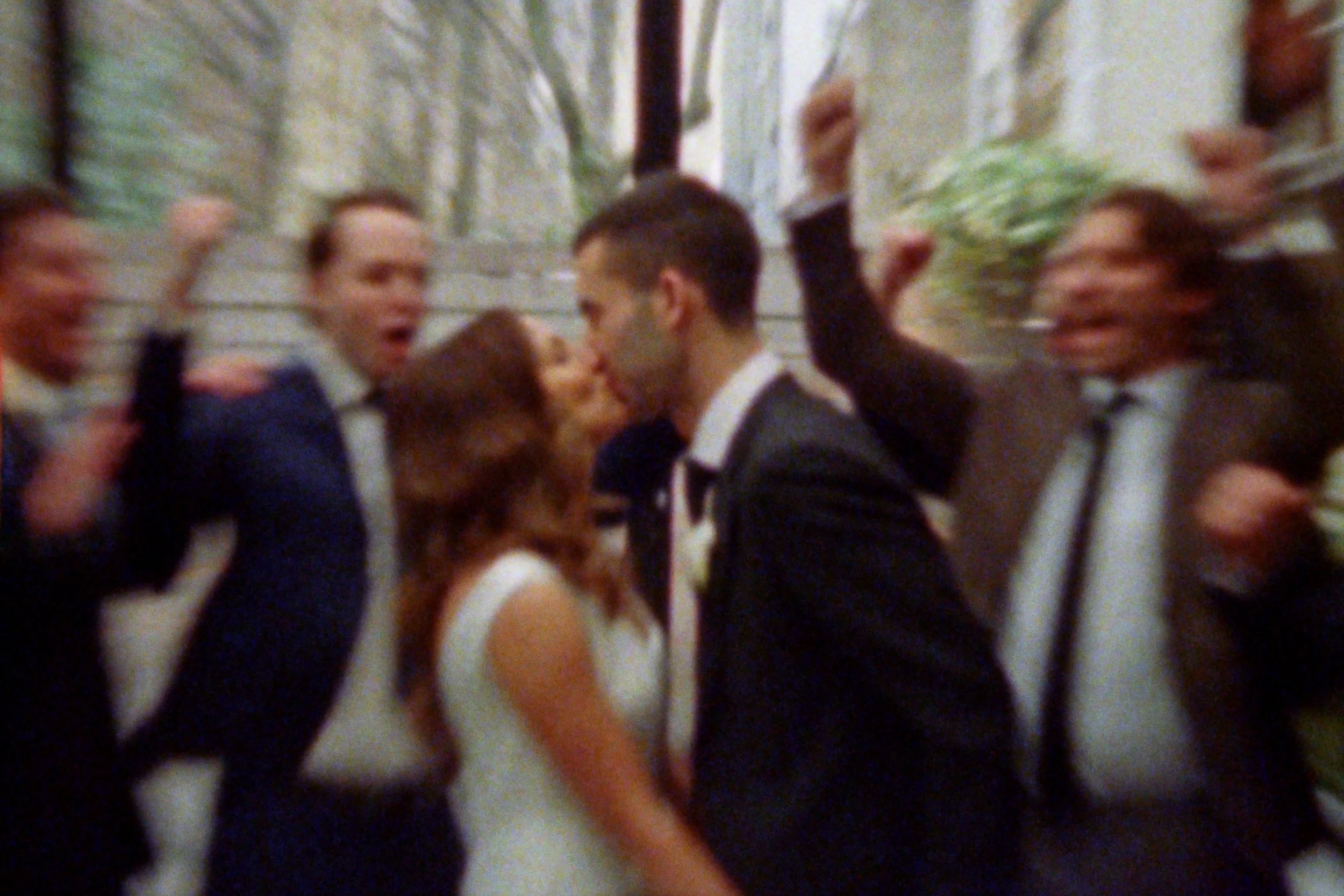 An artsy photo of bridal and groom at a wedding, with some engaged in conversation and kissing.