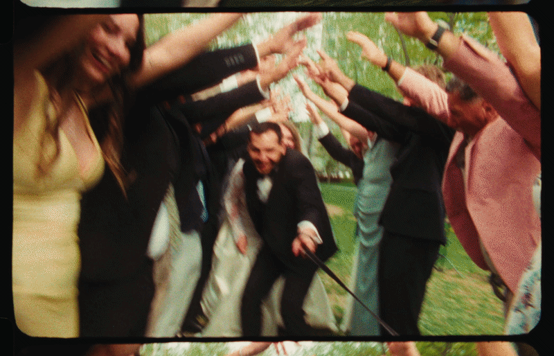 Group of people forming a tunnel with their hands, smiling, outdoors in a park with trees.