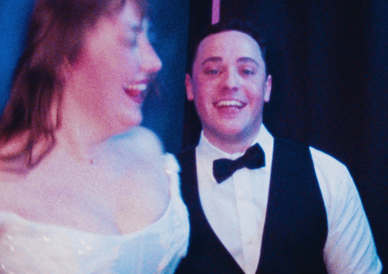 Two people dressed in formal attire, smiling and laughing at an event.