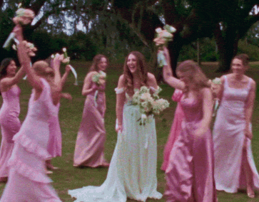 A bride in a white gown holding a bouquet surrounded by five bridesmaids in pink dresses celebrating outdoors at Oheka castle in New York