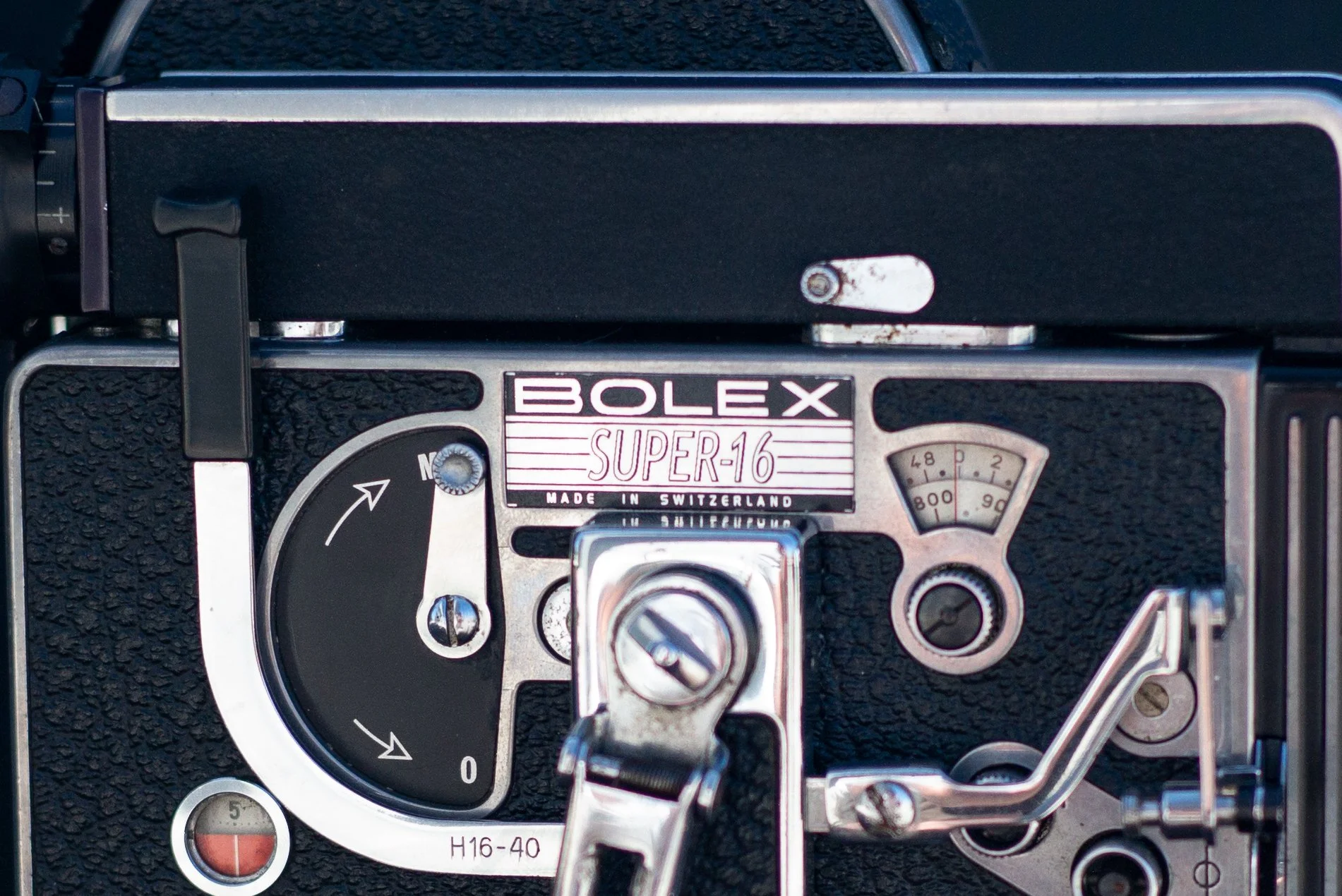 Close-up of the control panel of a vintage Bolex Super 16 film camera, showing dials, levers, and a label with Swiss origin.