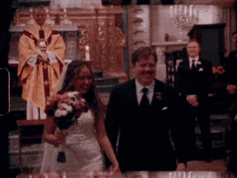 A wedding ceremony in a church with a bride holding a bouquet and a groom in a suit, accompanied by a priest and another person in formal attire.