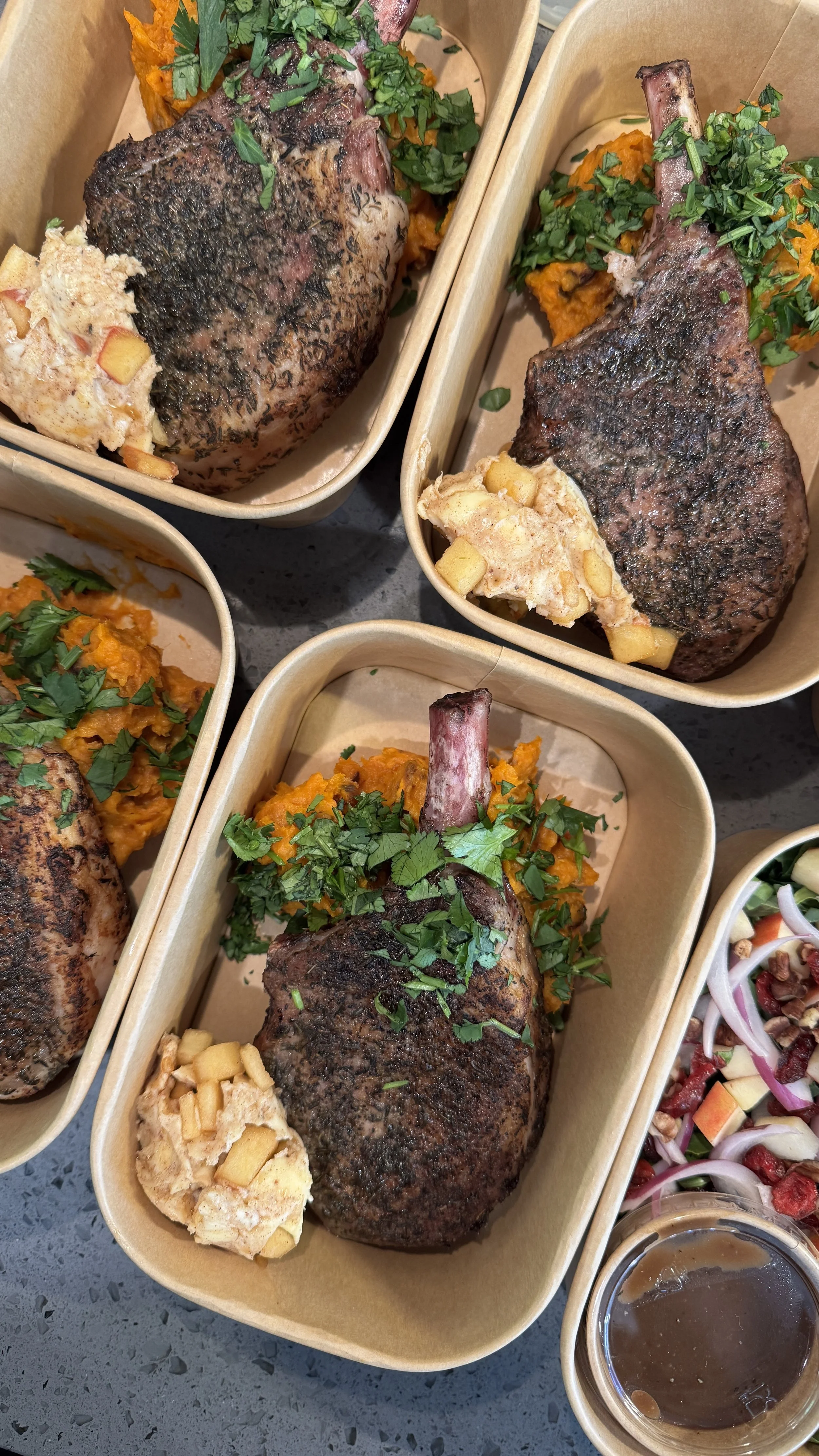 Multiple servings of large beef steaks topped with chopped herbs, served with sweet potato mash and a side of vegetable salad with radicchio and onion, and a small cup of brown gravy.