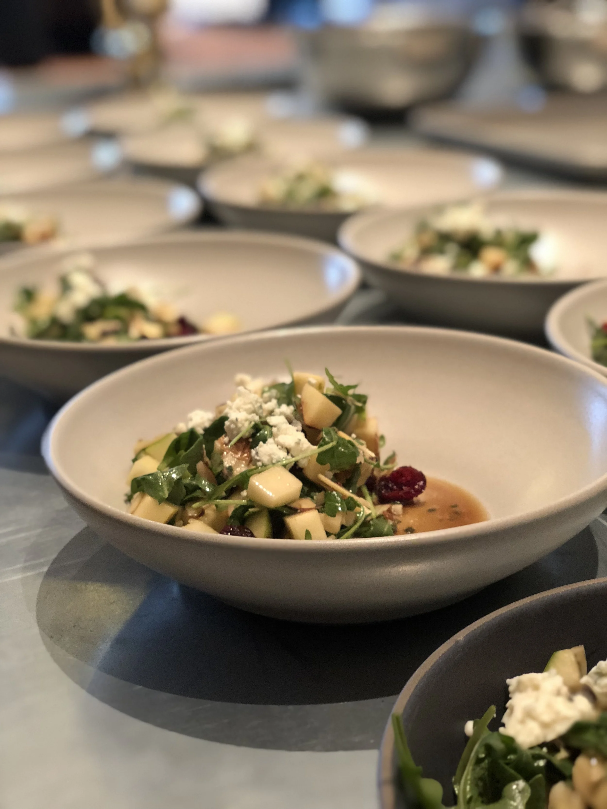 Multiple bowls of salad with greens, cheese, and dried berries, arranged on a table.