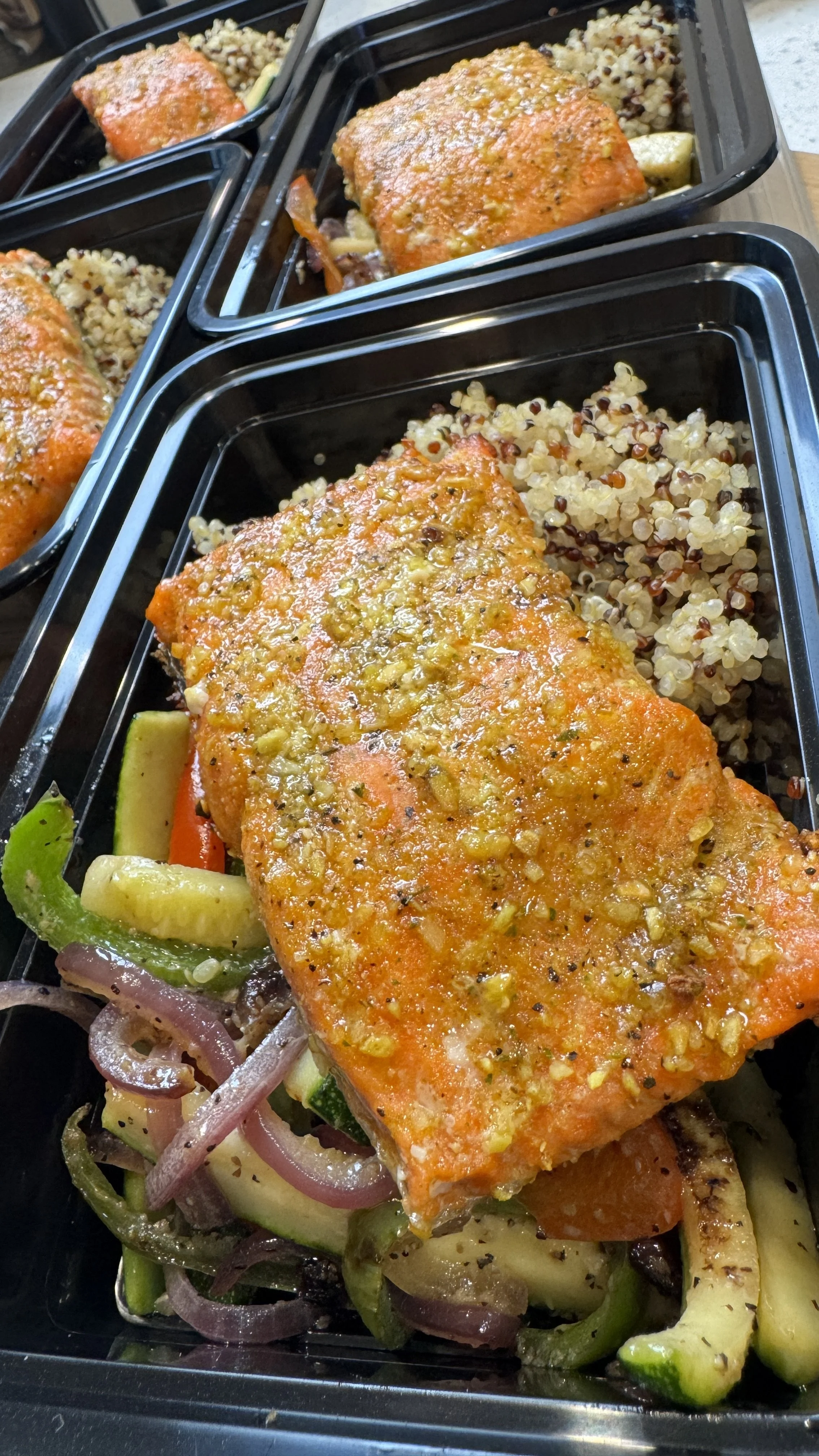Baked salmon fillets with seasoned crust, served with grilled vegetables including zucchini, bell peppers, and onions, alongside a side of cooked quinoa.