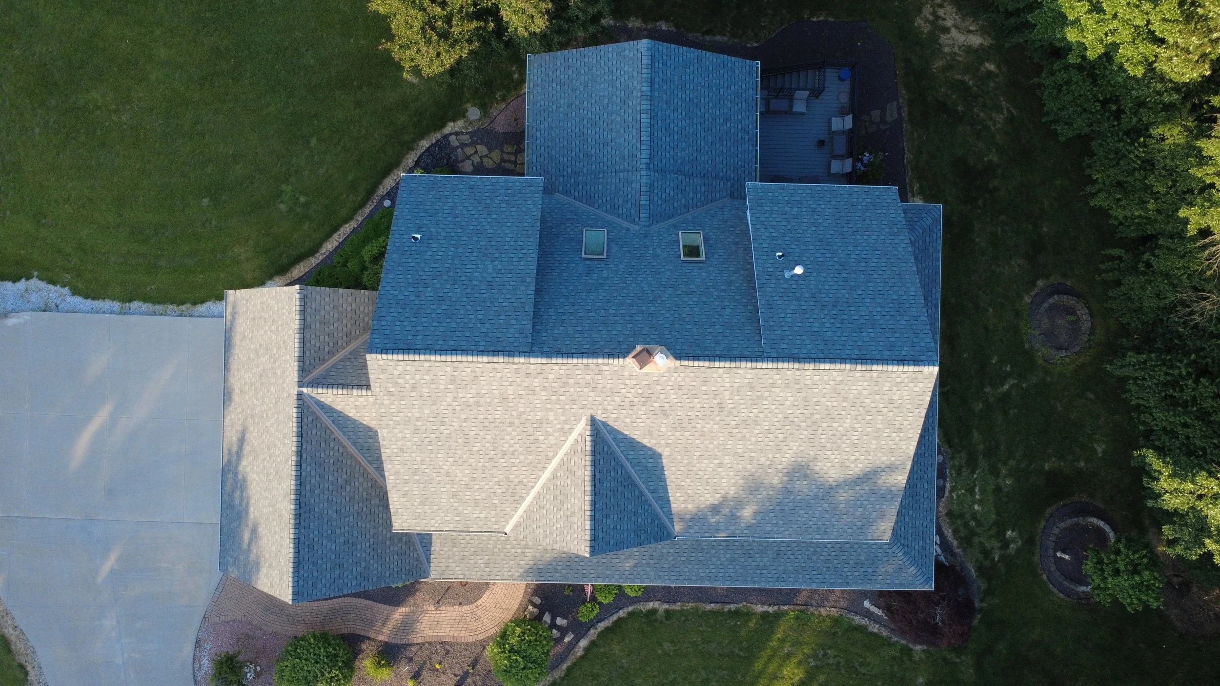 Aerial view of a house with a gray roof, surrounded by green trees and landscaped yard.