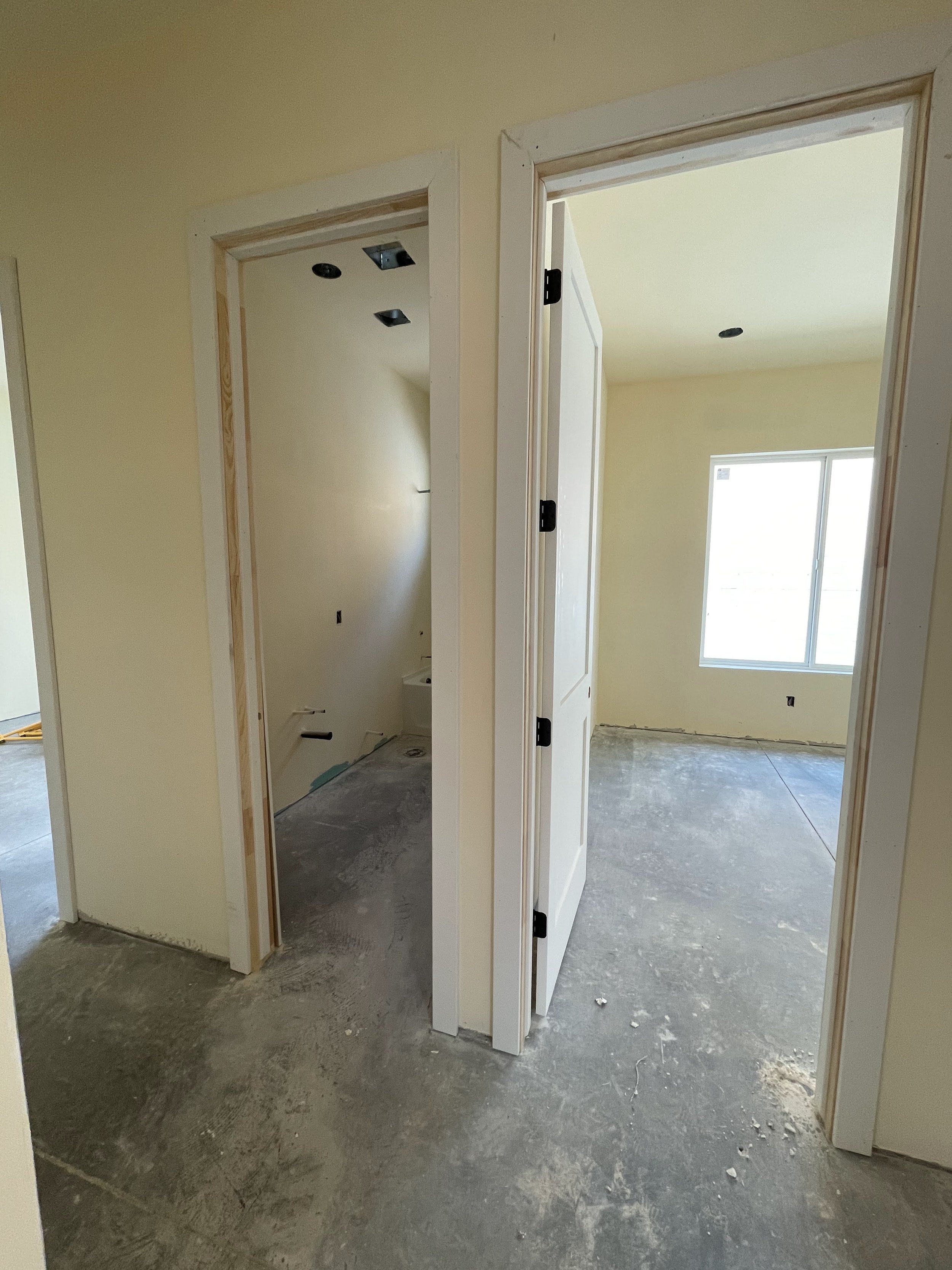 Interior view of a house under construction with unfinished floors, walls painted light yellow, and open doorways leading to rooms.