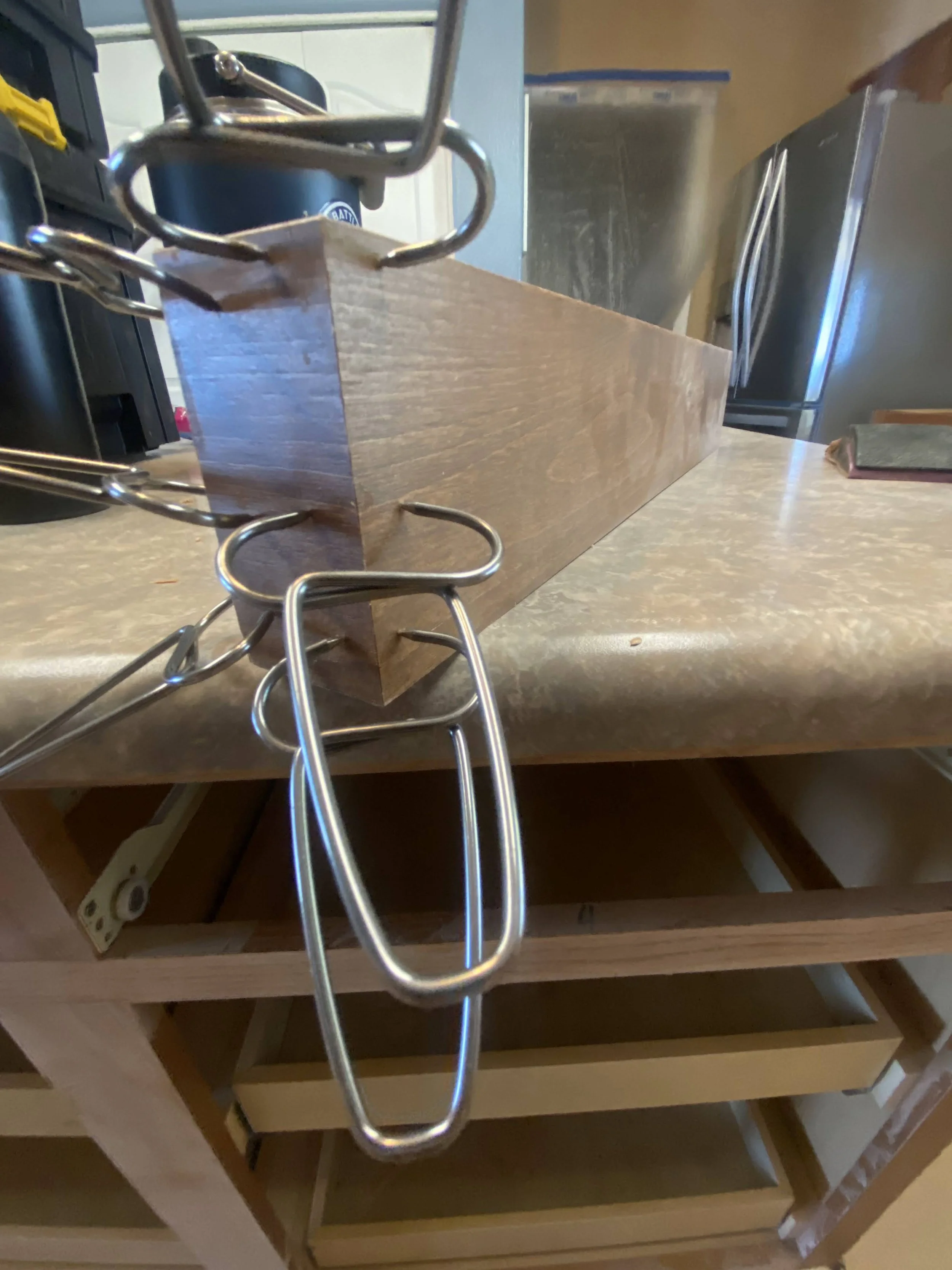 A wooden drawer with metal handles inside a kitchen cabinet, with a chain hanging from the top of the drawer.