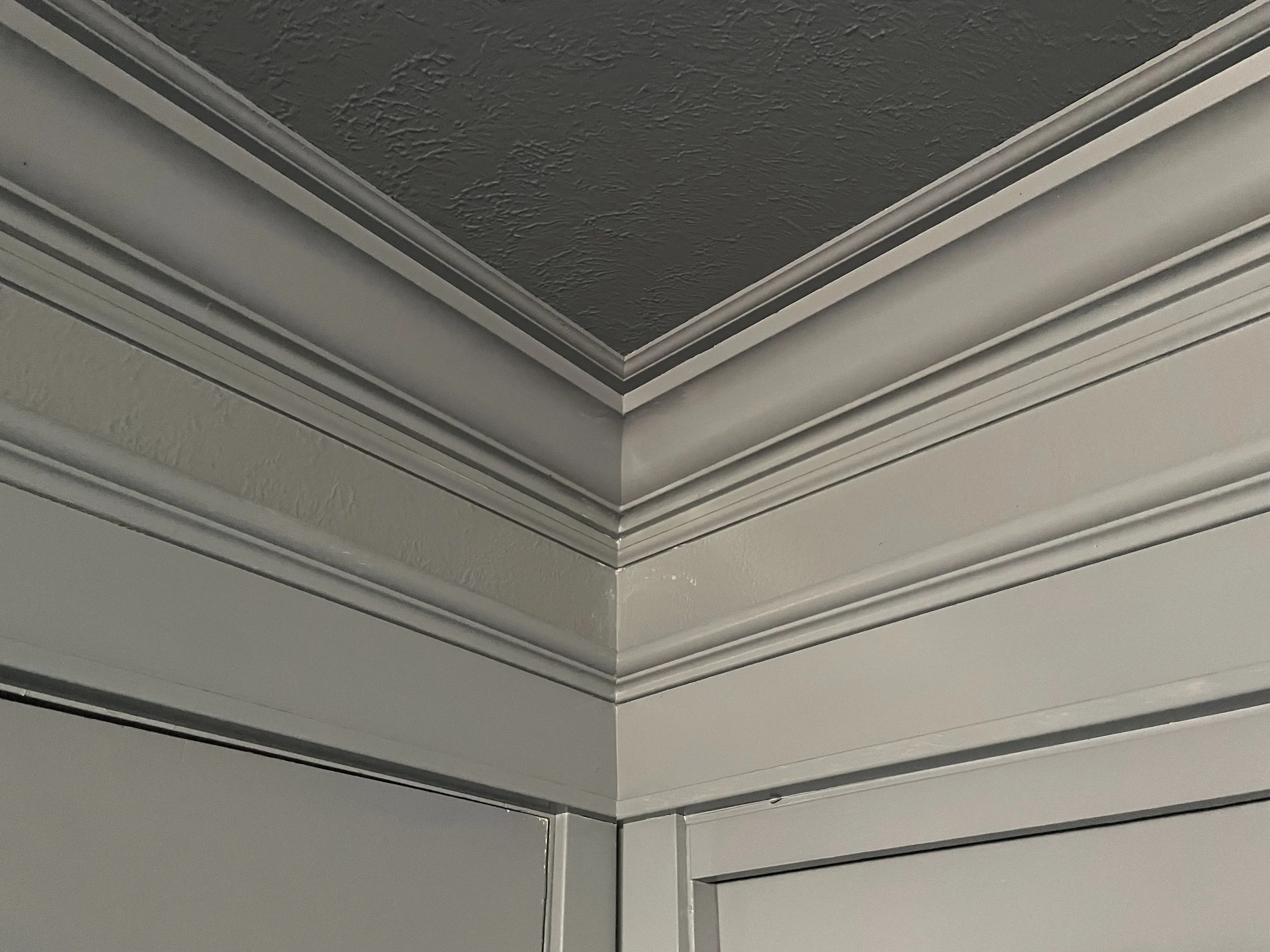 The image shows a close-up of a ceiling corner with crown molding and textured ceiling paint.