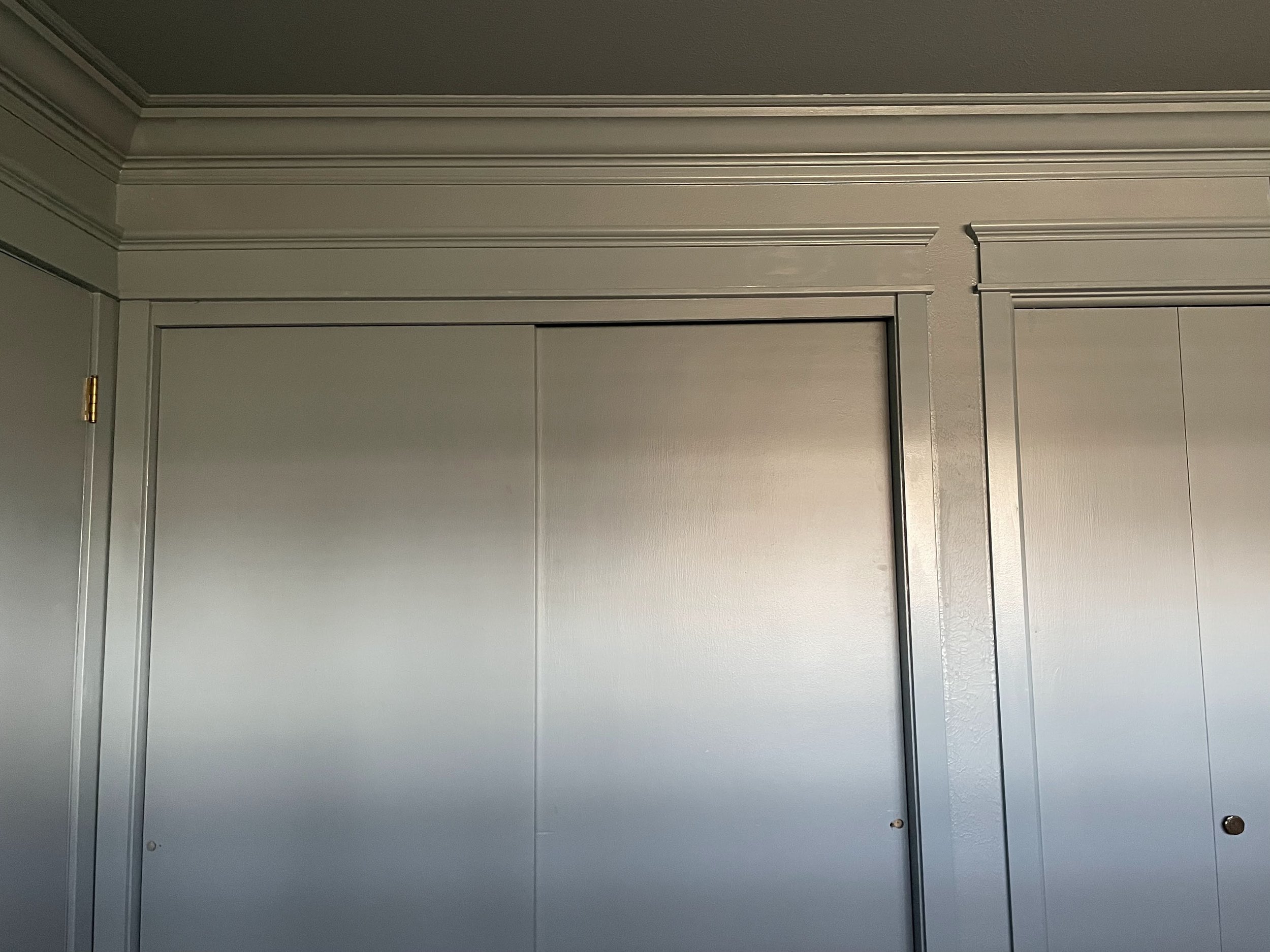 Close-up of a silver-colored cabinet or door with decorative crown molding at the top and a small round keyhole in the bottom right corner.
