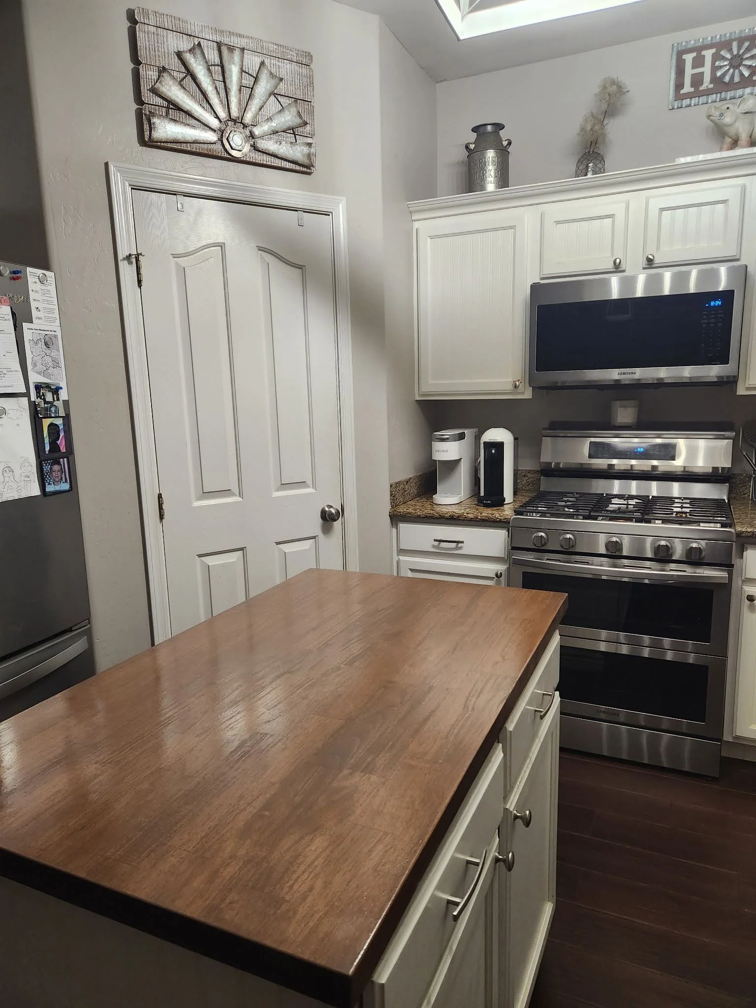 A kitchen countertop with a wooden surface, situated in front of white cabinets, with a stainless steel stove, microwave, and other appliances visible along the wall.