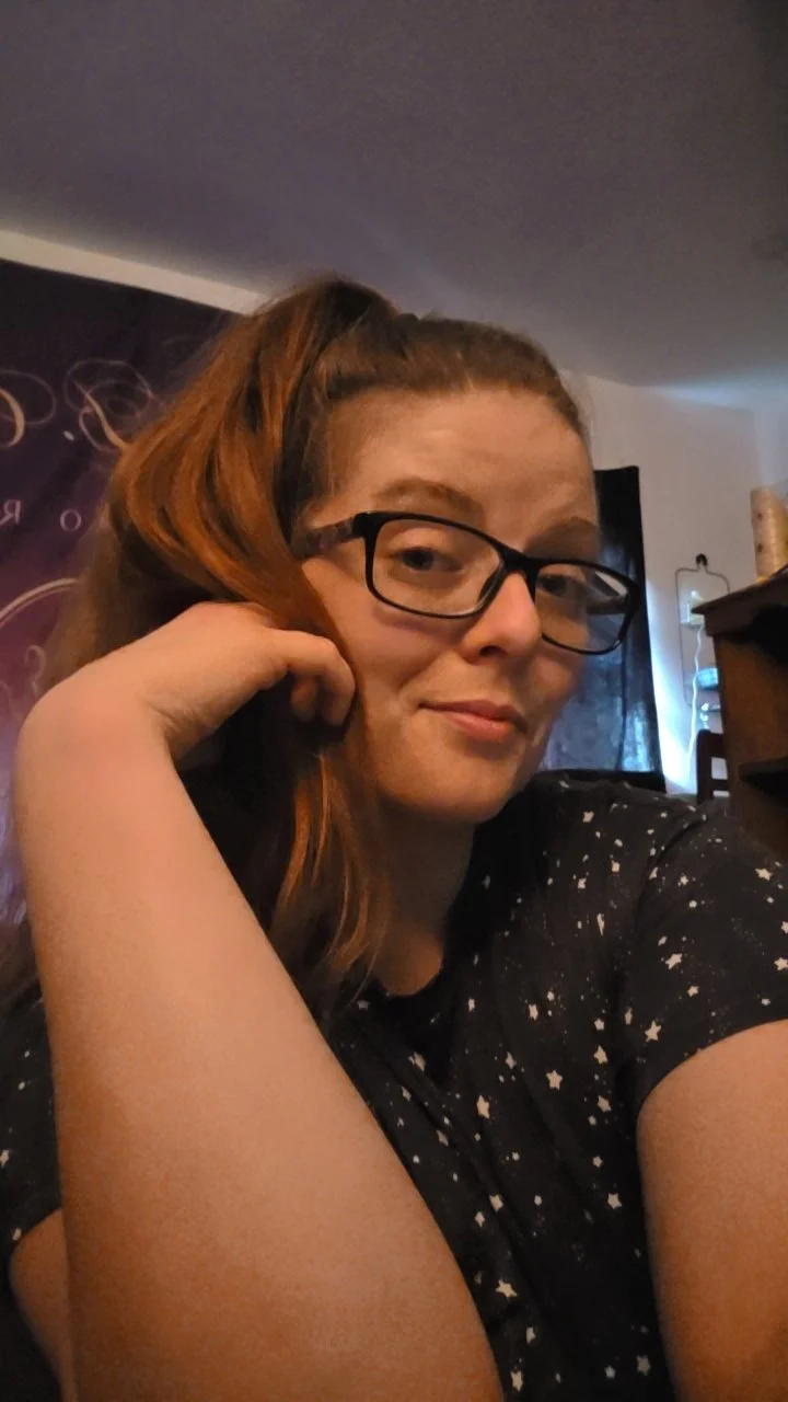 Woman with glasses and a ponytail posing indoors in a black star-patterned shirt