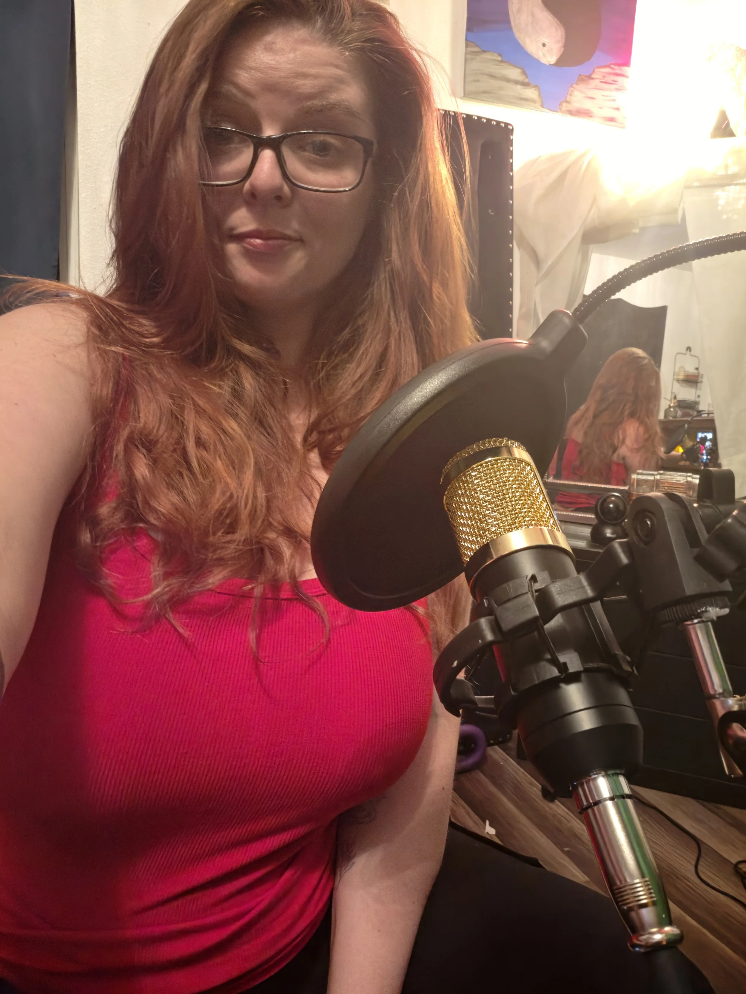 Woman wearing glasses and a bright pink sweater speaking into a studio microphone