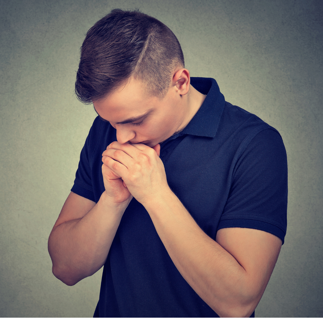 A young man with short, styled hair, wearing a black polo shirt, appears to be praying with his hands clasped and head bowed against a plain, neutral background.