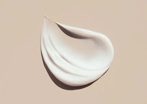 A white dollop of cream or lotion on a beige background.