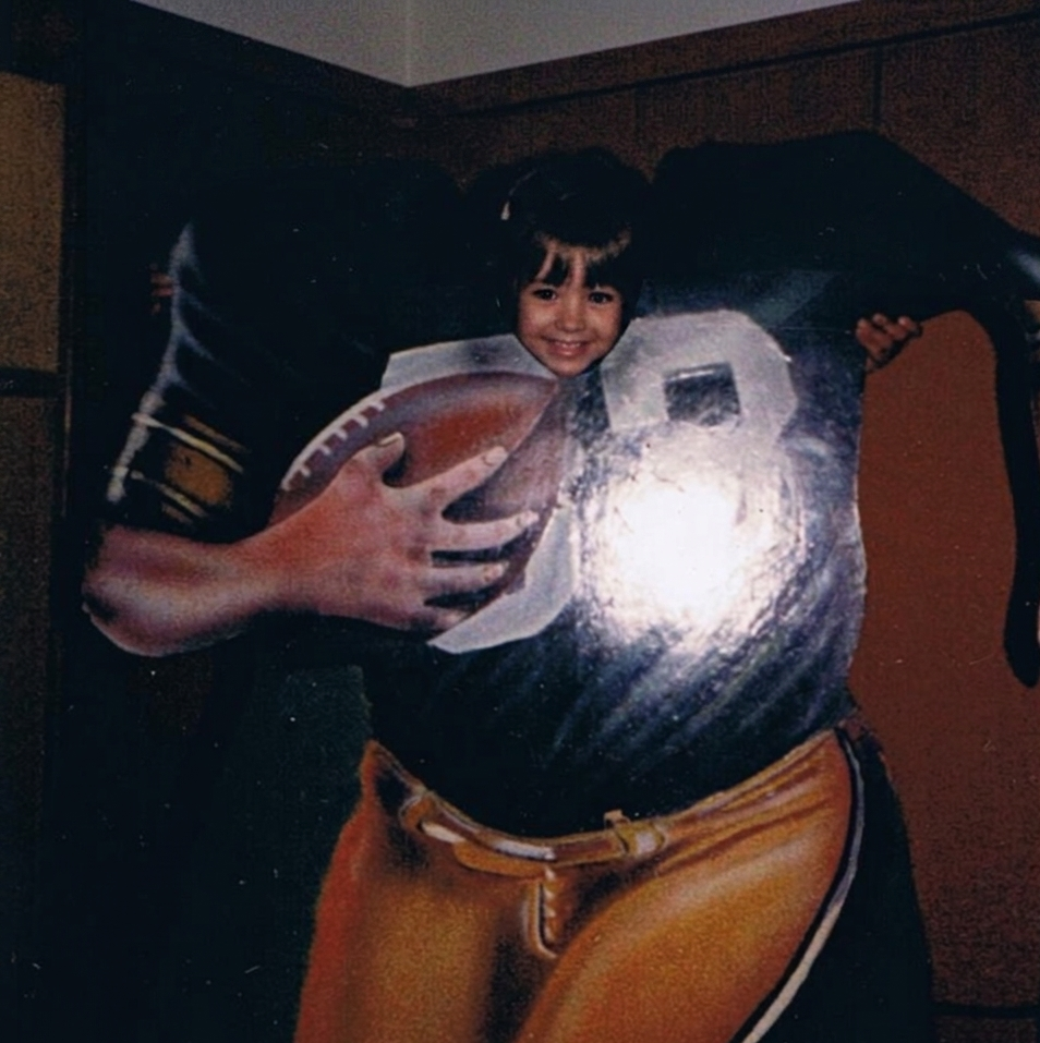 Child holding a football, standing with a Minnesota Vikings jersey, smiling