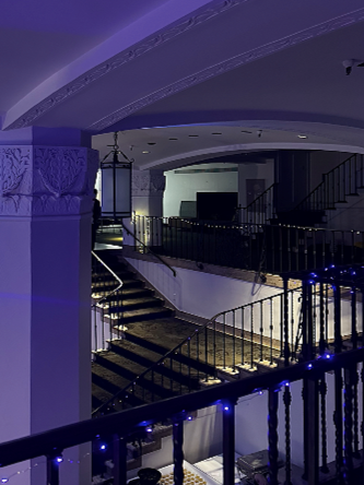 Interior of a building featuring a staircase with black railings and blue lights, decorative columns, and a curved ceiling.