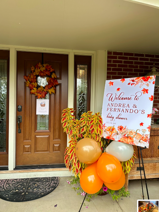 Decorations for a baby shower in front of a wooden door with a fall wreath and a welcome sign for Andrea and Fernando's baby shower, featuring balloons and autumn-themed flowers.
