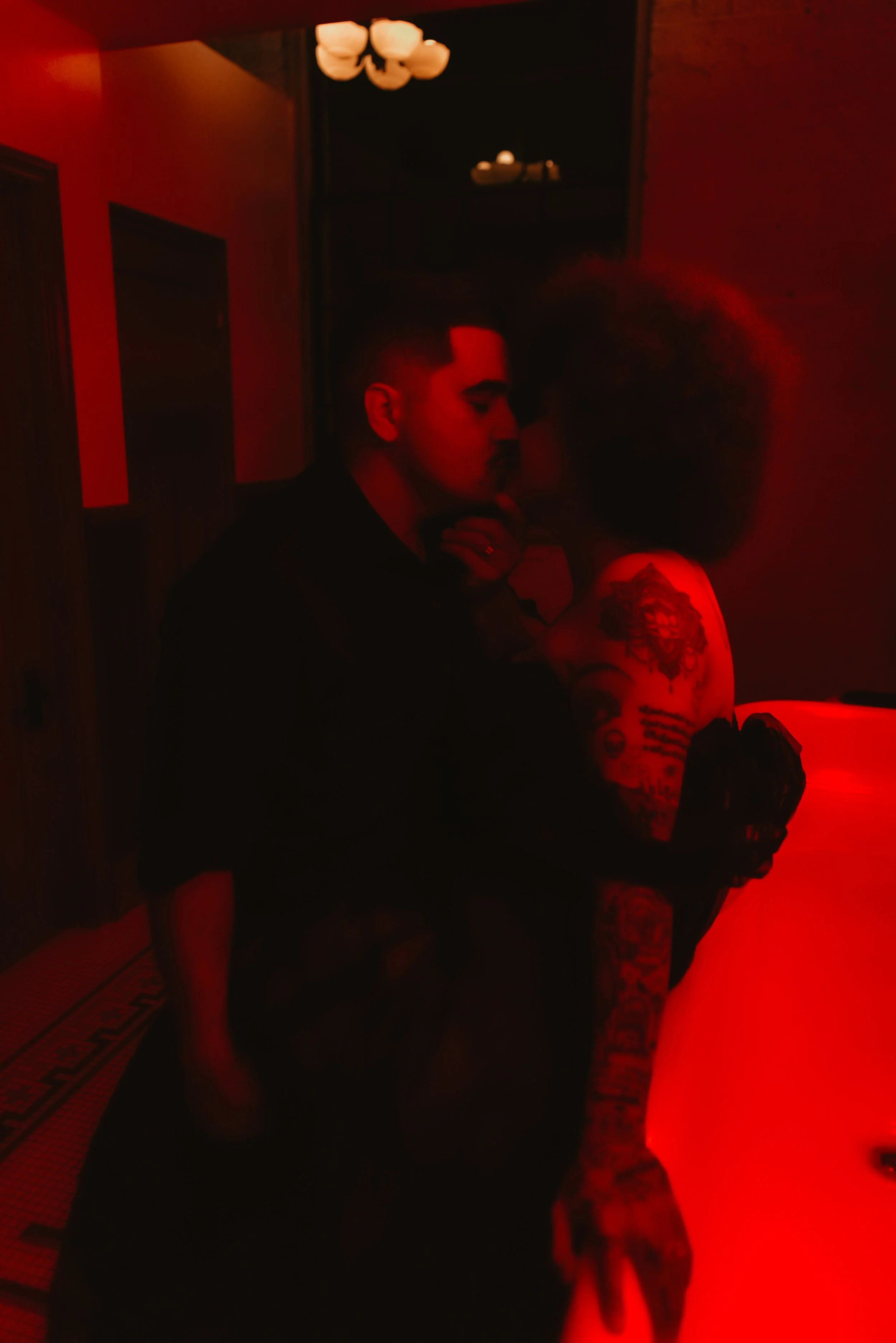 Newlywed couple kissing in a bathroom with red ambient lighting