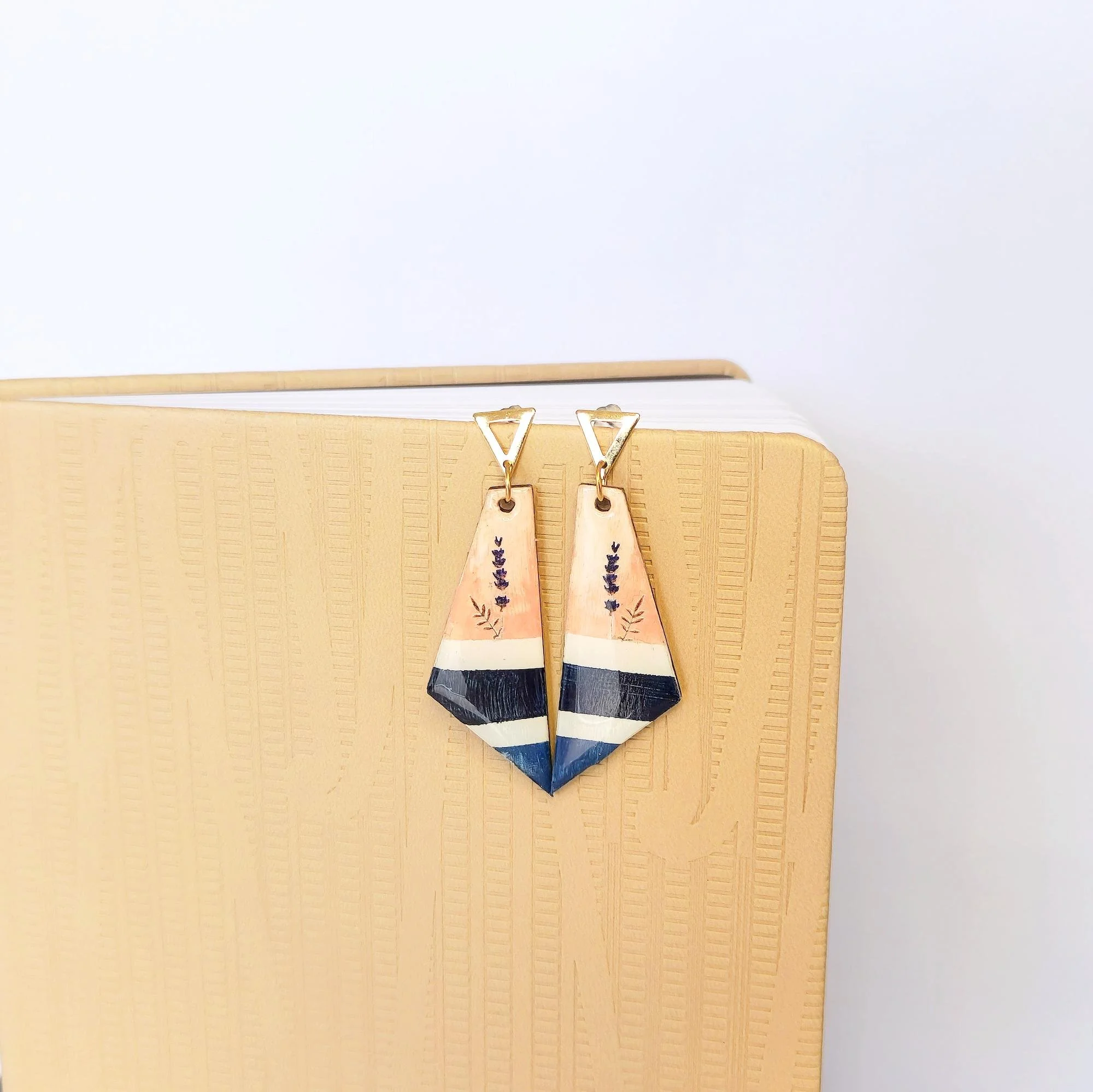 Colorful geometric earrings with painted floral designs hanging on a beige-colored stand.
